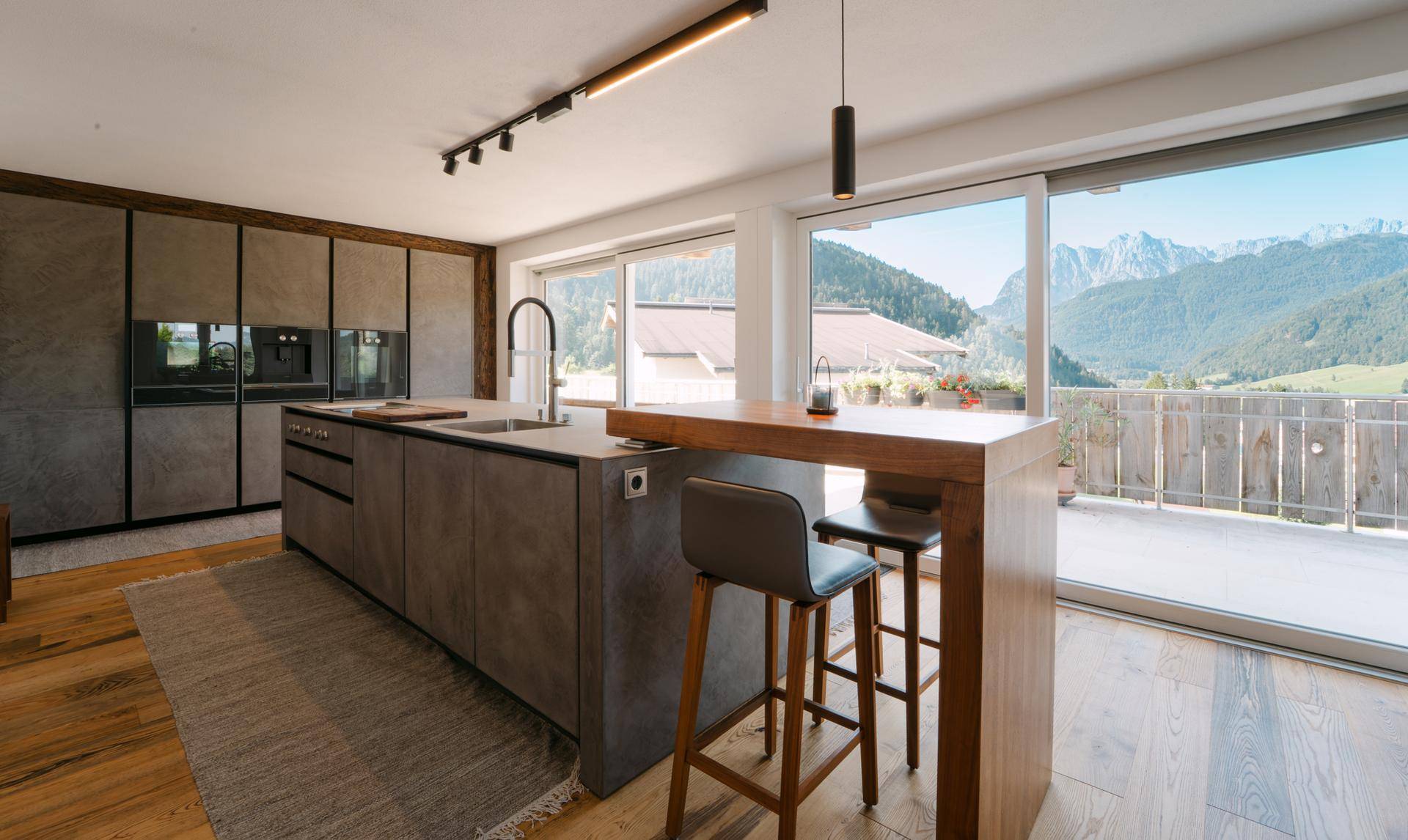 Moderne Küche mit Kochinsel, Frühstücksbar und Zugang zu einer Terrasse mit Bergblick.