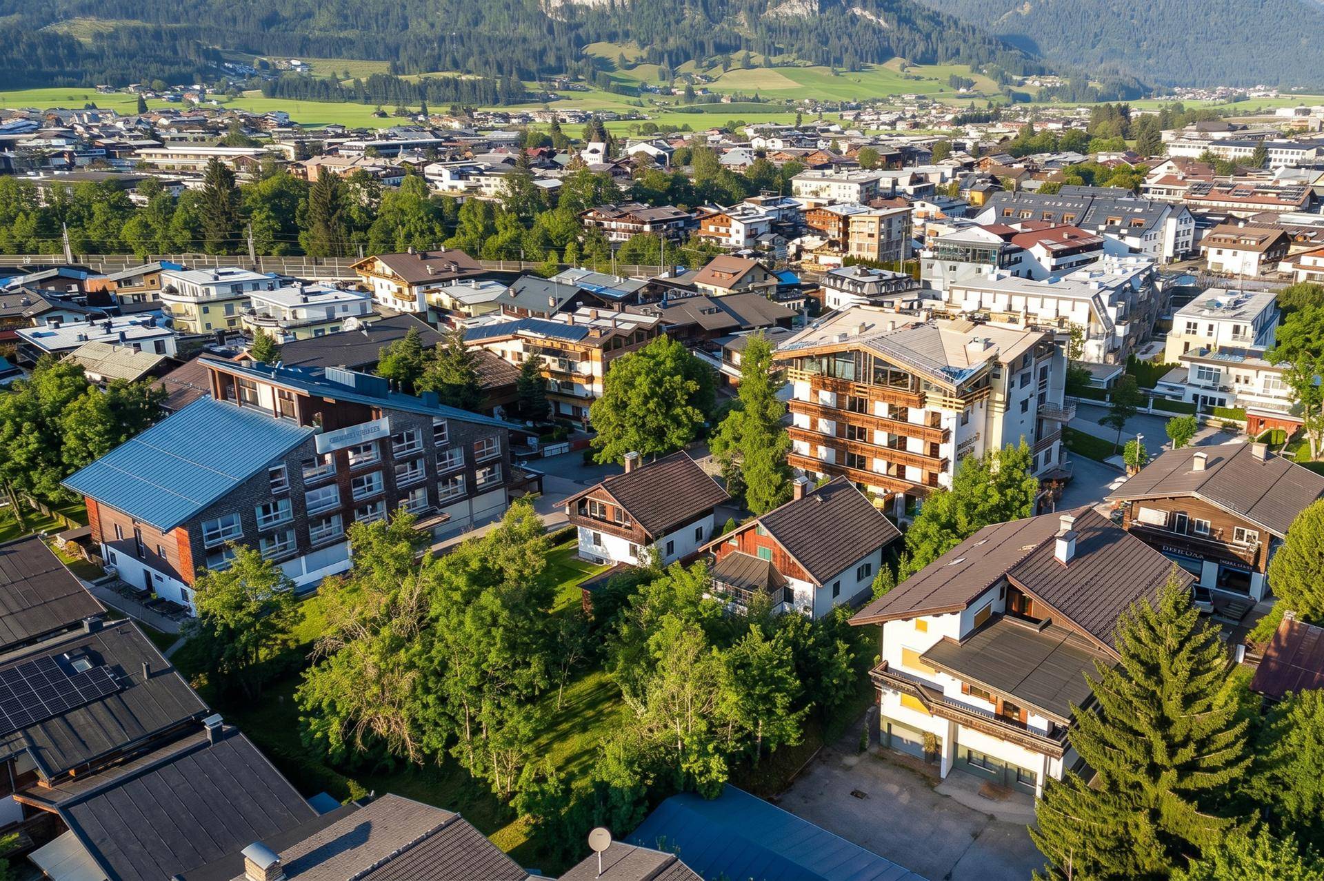 Weitläufige Luftaufnahme einer Siedlung mit vielfältigen Gebäuden, umgeben von grünen Feldern und Bergen.