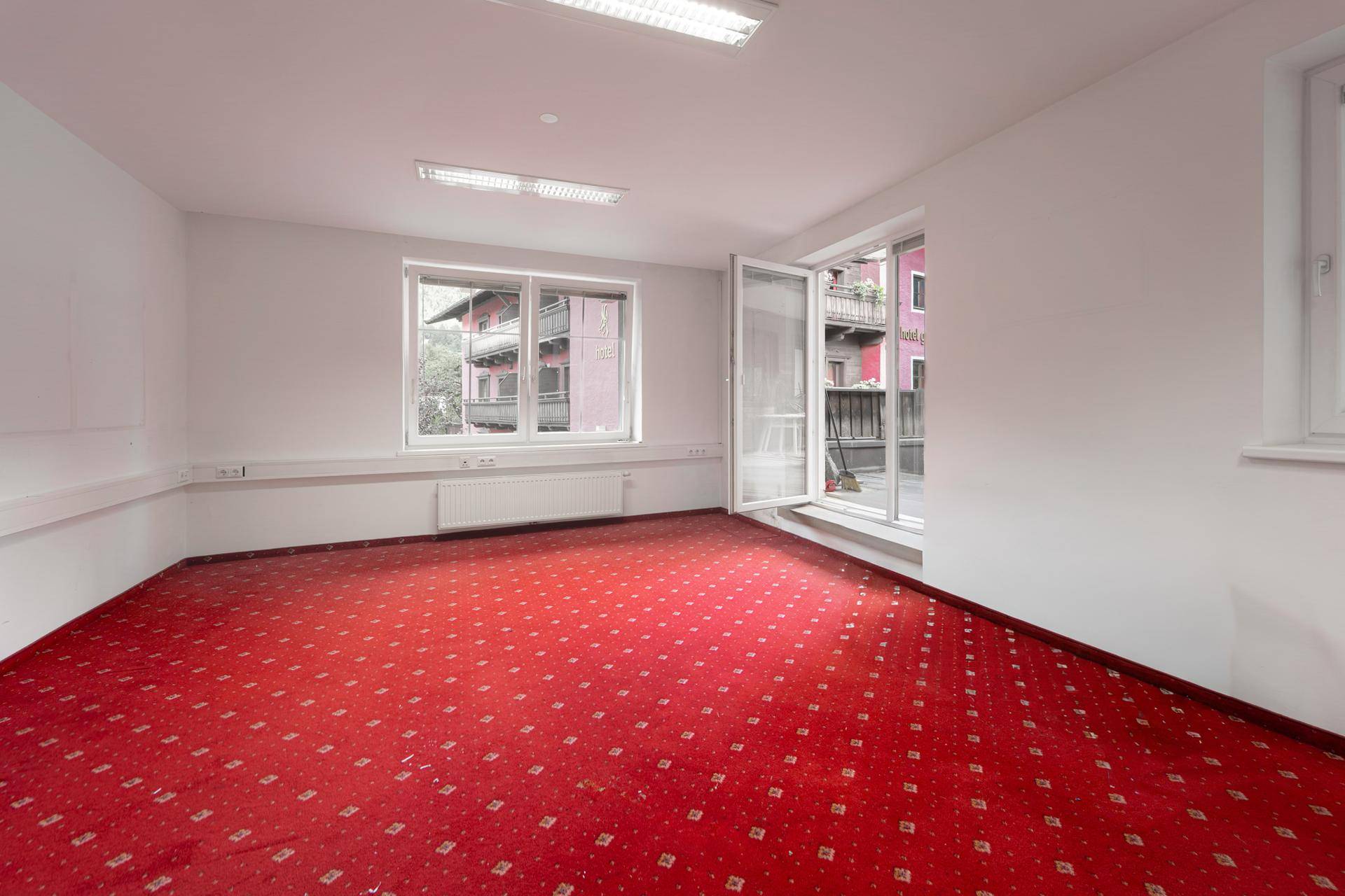 Geräumiges Büro mit rotem Teppichboden und Zugang zu einem französischen Balkon.
