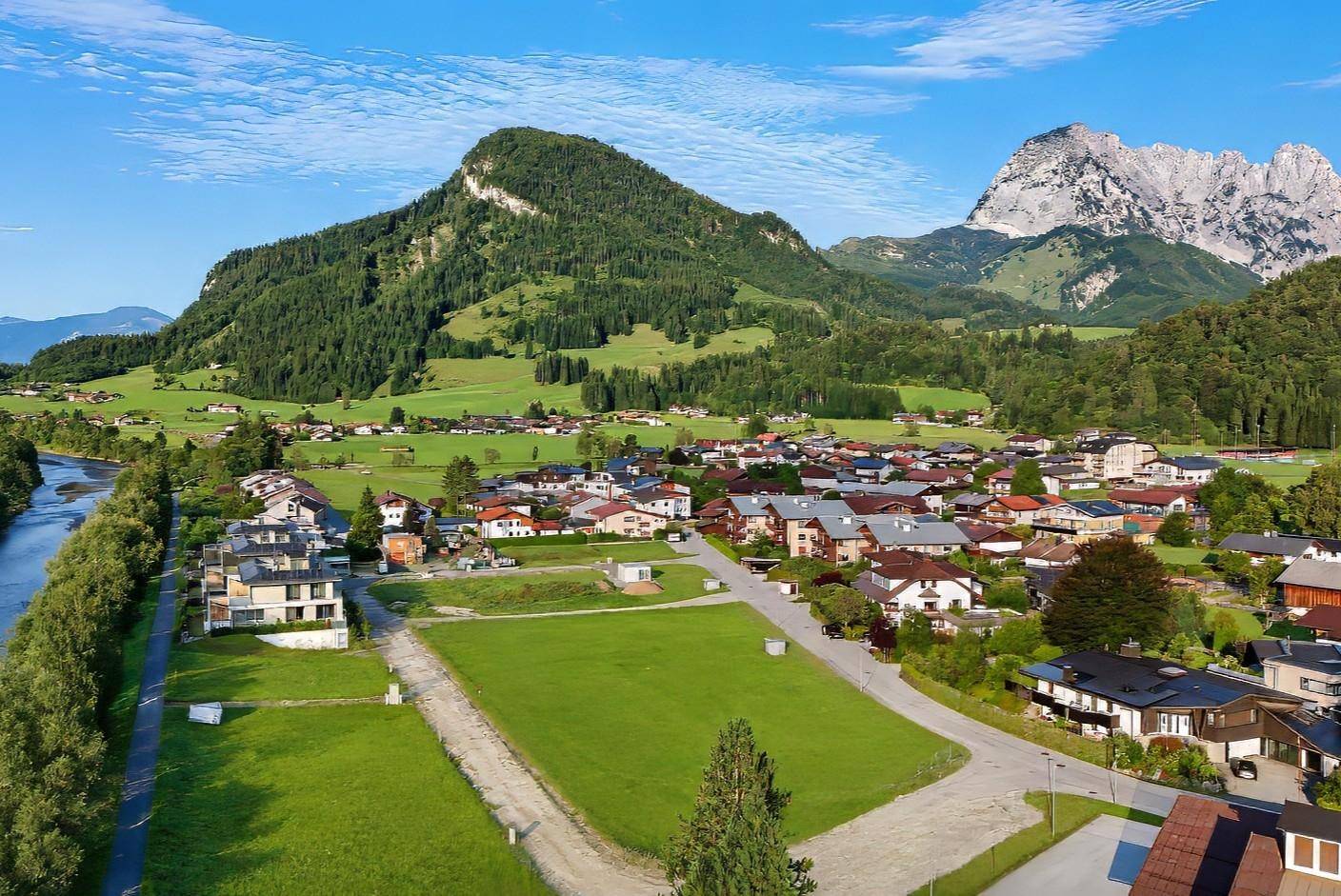 Luftaufnahme eines Dorfes in einer malerischen Berglandschaft mit Fluss und grünen Hügeln.