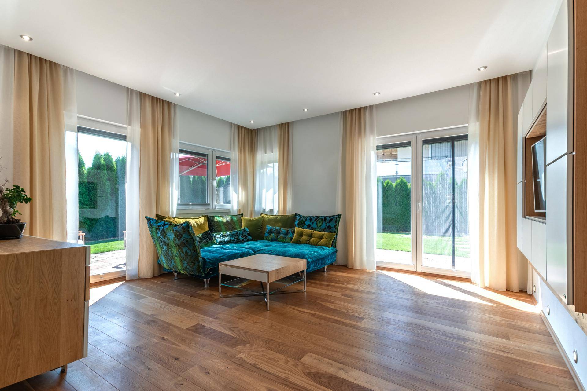 Helles Wohnzimmer mit Holzboden, farbenfrohem Sofa und Zugang zum Garten durch große Türen.