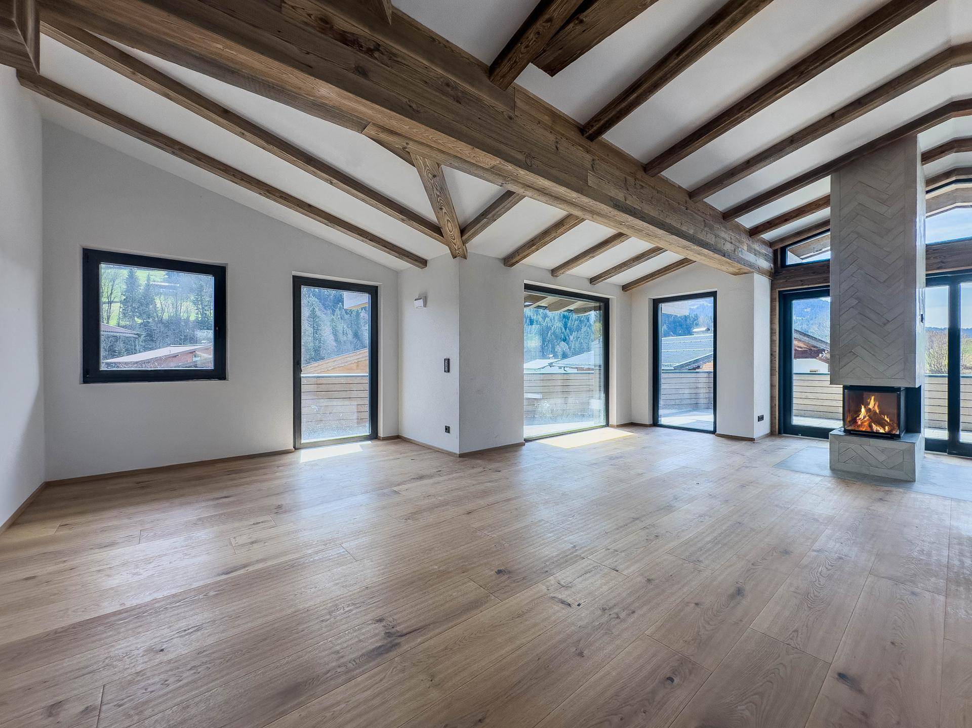 Geräumiges Wohnzimmer mit sichtbaren Holzbalken, modernem Kamin und großen Fenstern mit Bergblick.