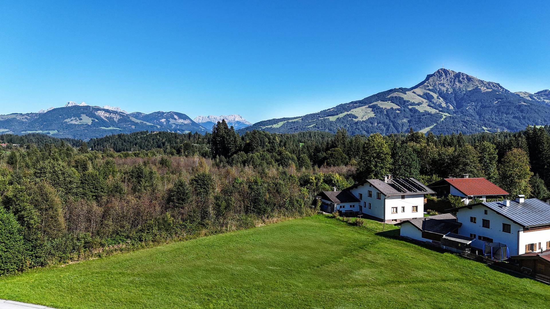 Panoramablick auf eine idyllische Wohnsiedlung umgeben von grünen Hügeln und fernen Bergen.