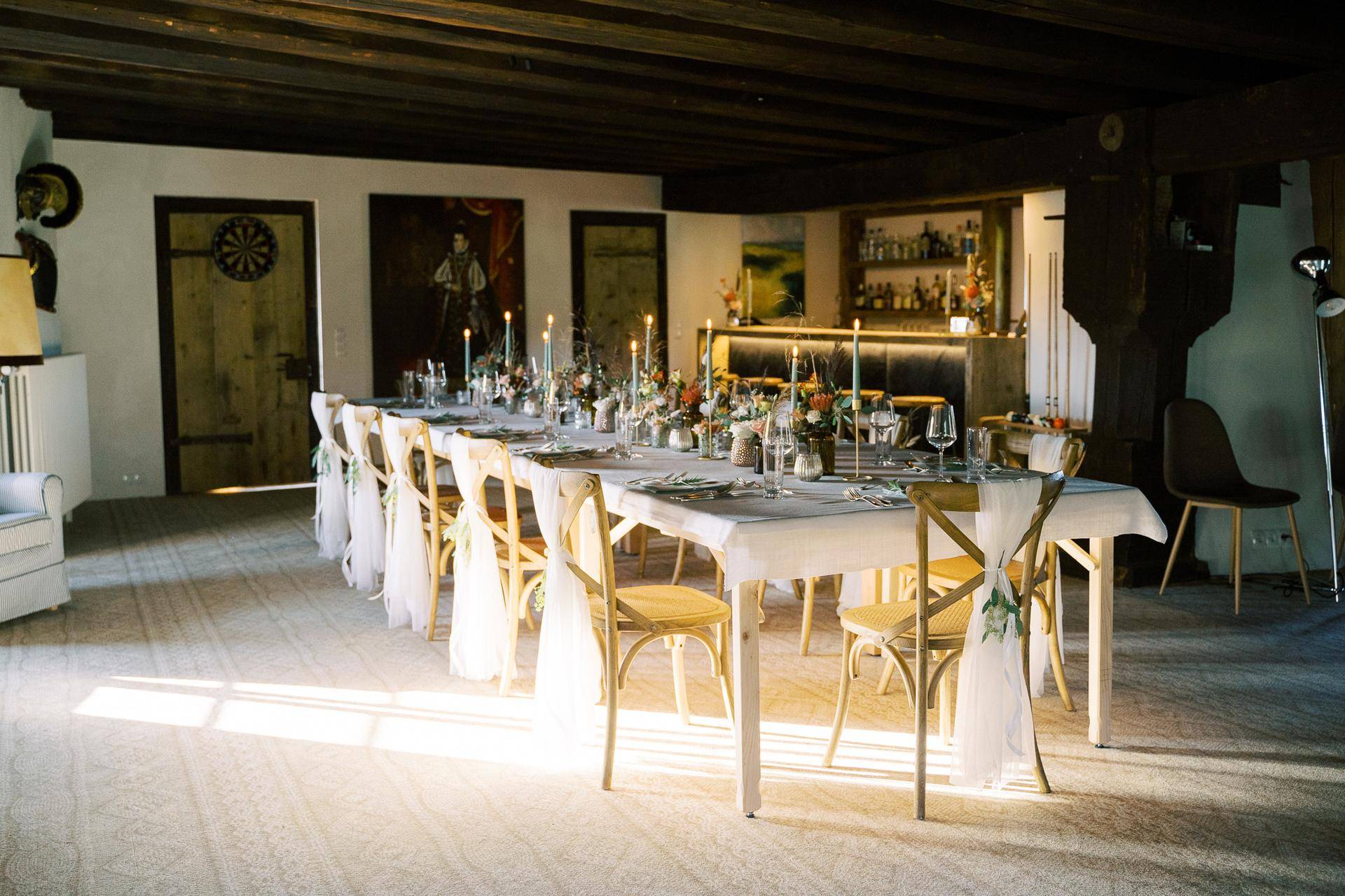 Großer Speisesaal mit langer Tafel, Holzbalkendecke und einer Bar im Hintergrund.