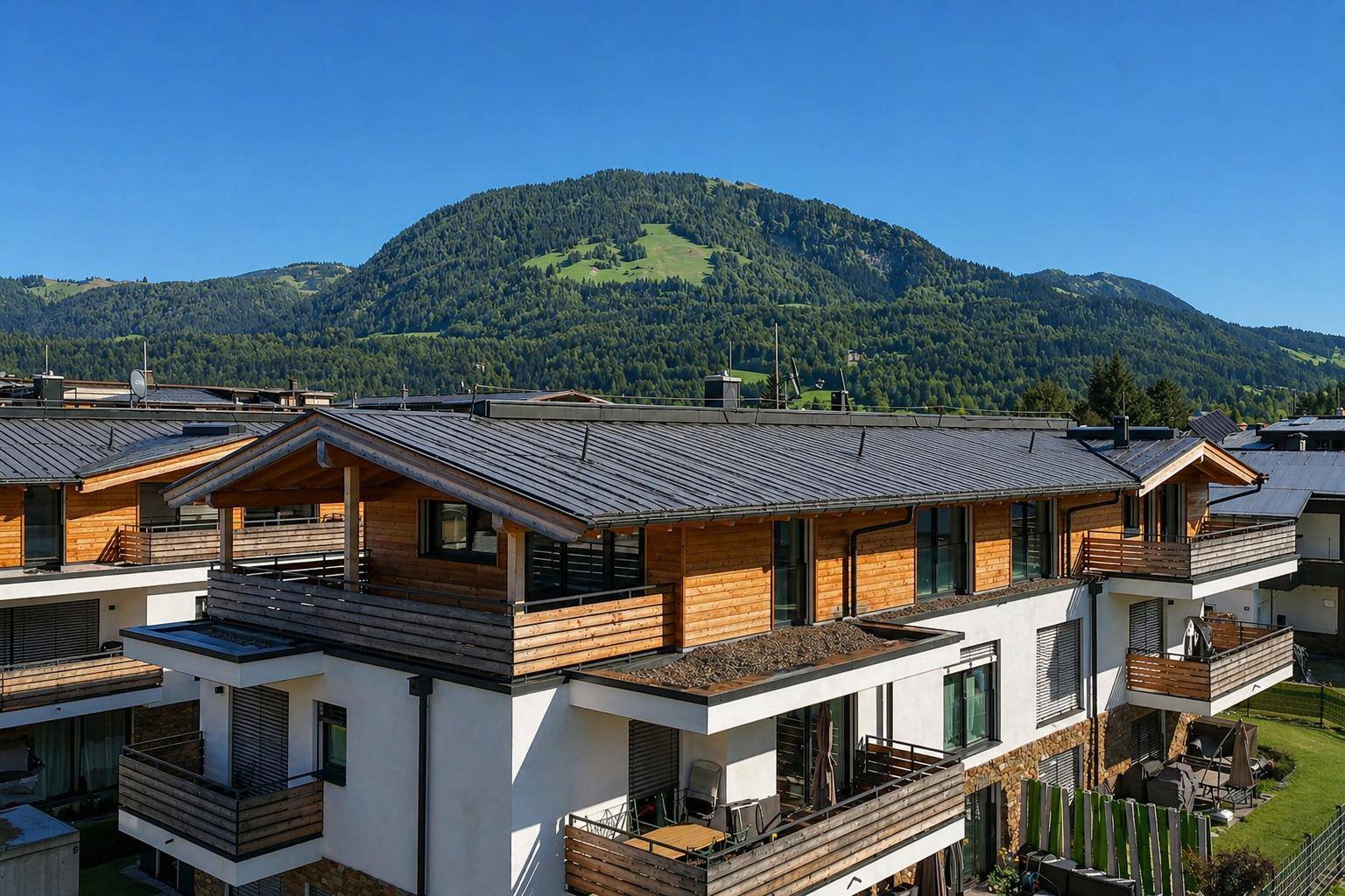 Reihe moderner Gebäude mit Holzverkleidung und Balkonen, eingebettet in eine grüne Berglandschaft.