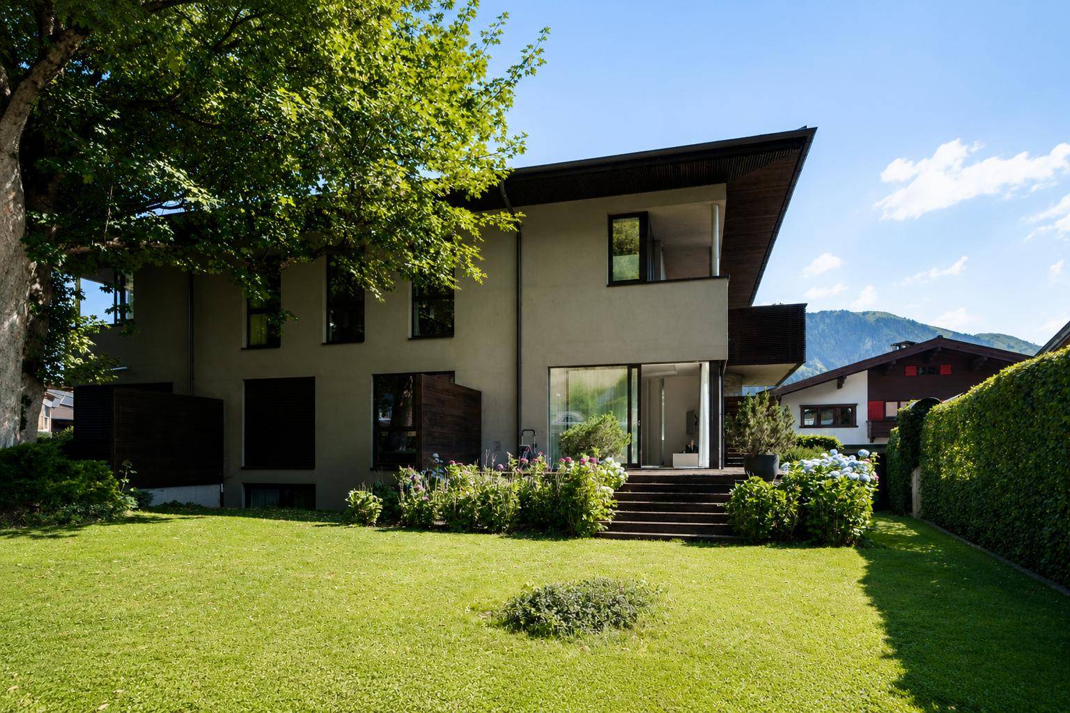 Modernes Einfamilienhaus mit gepflegtem Rasen, Bäumen und Sträuchern im Gartenbereich.