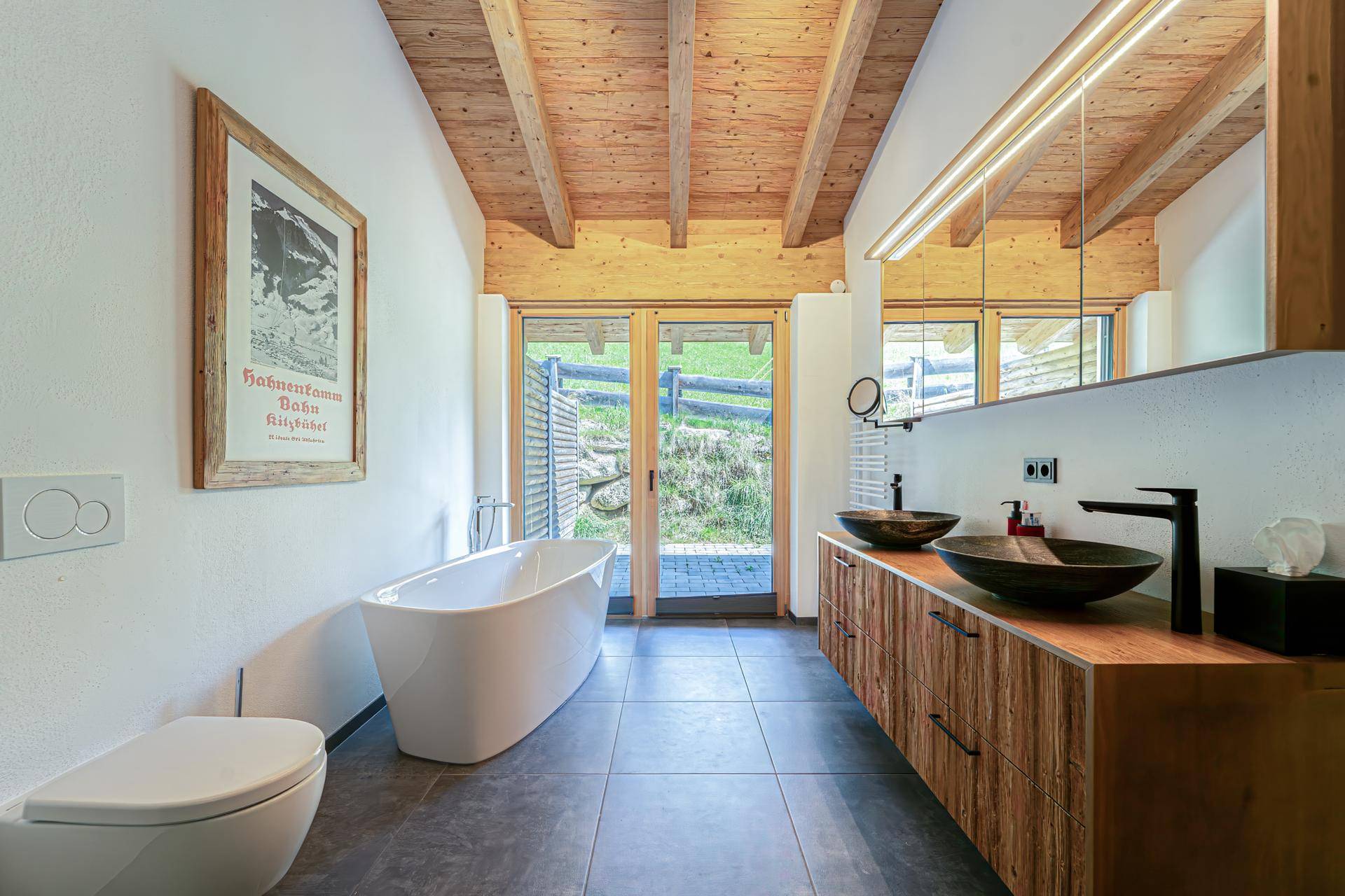 Modernes Badezimmer mit freistehender Badewanne, Doppelwaschbecken und Holzelementen, mit Zugang nach draußen.