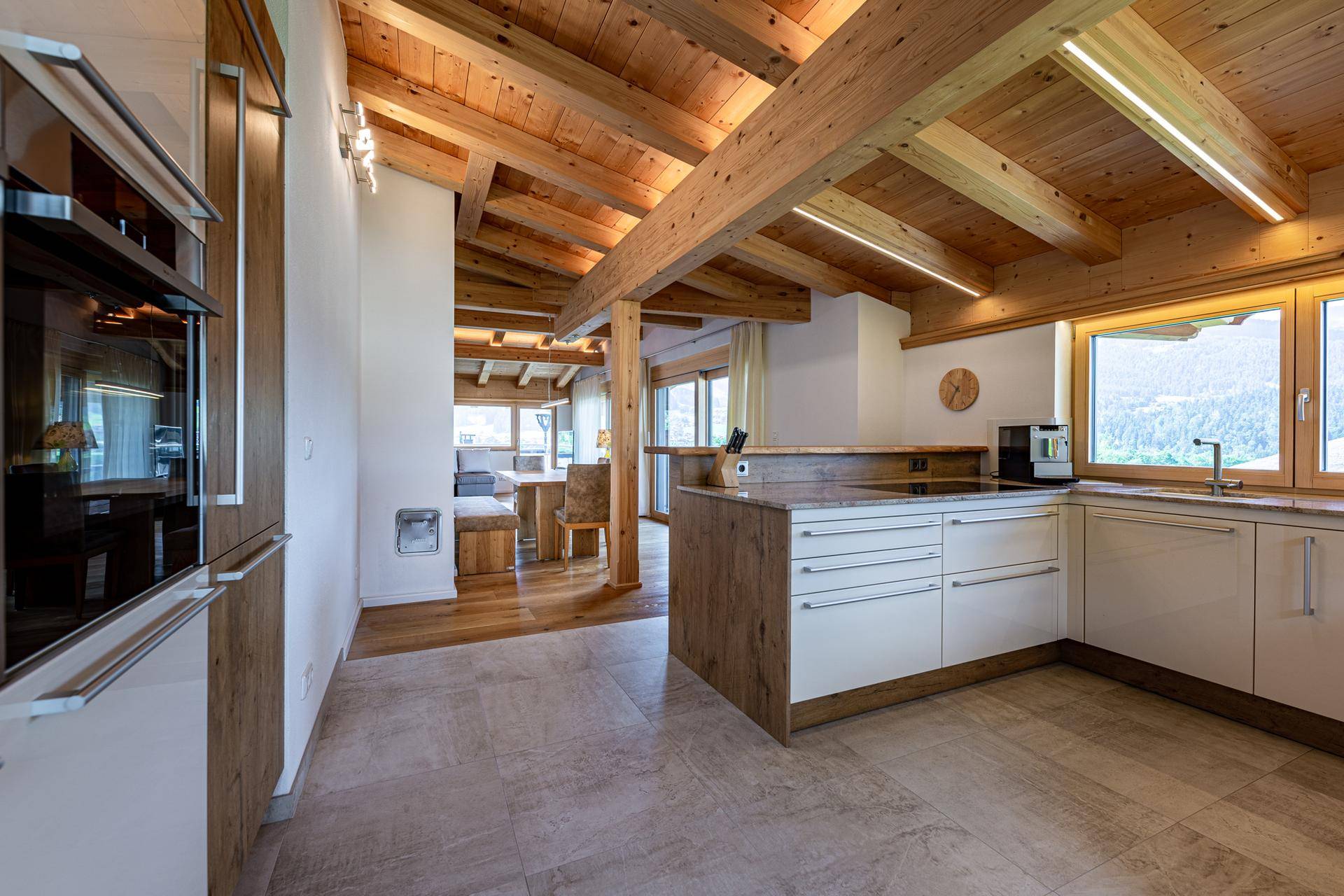 Moderne Küche mit Holzbalkendecke, Kücheninsel und Blick in den Essbereich.