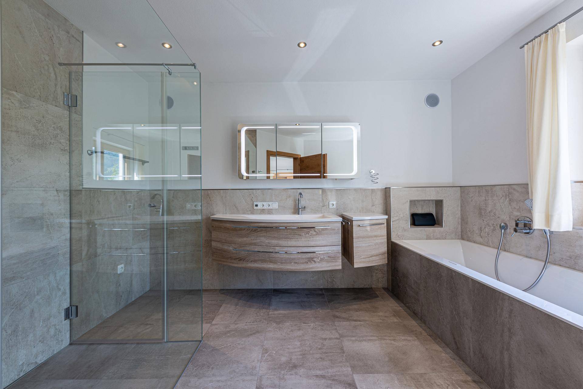 Modernes Badezimmer mit begehbarer Dusche, Badewanne und beleuchtetem Spiegelschrank.