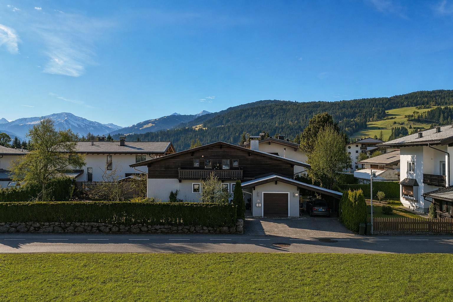 Charmantes Einfamilienhaus mit Holzfassade, Garage und Carport vor alpiner Bergkulisse.