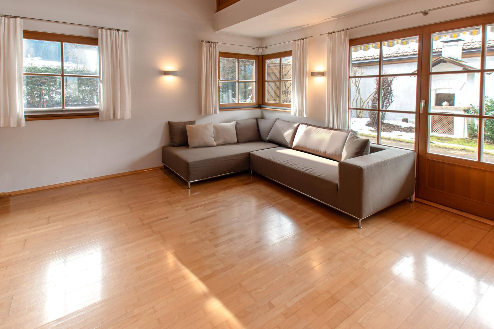 Helles Wohnzimmer mit Holzparkett, bequemer Eckcouch und Zugang zum Gartenbereich.