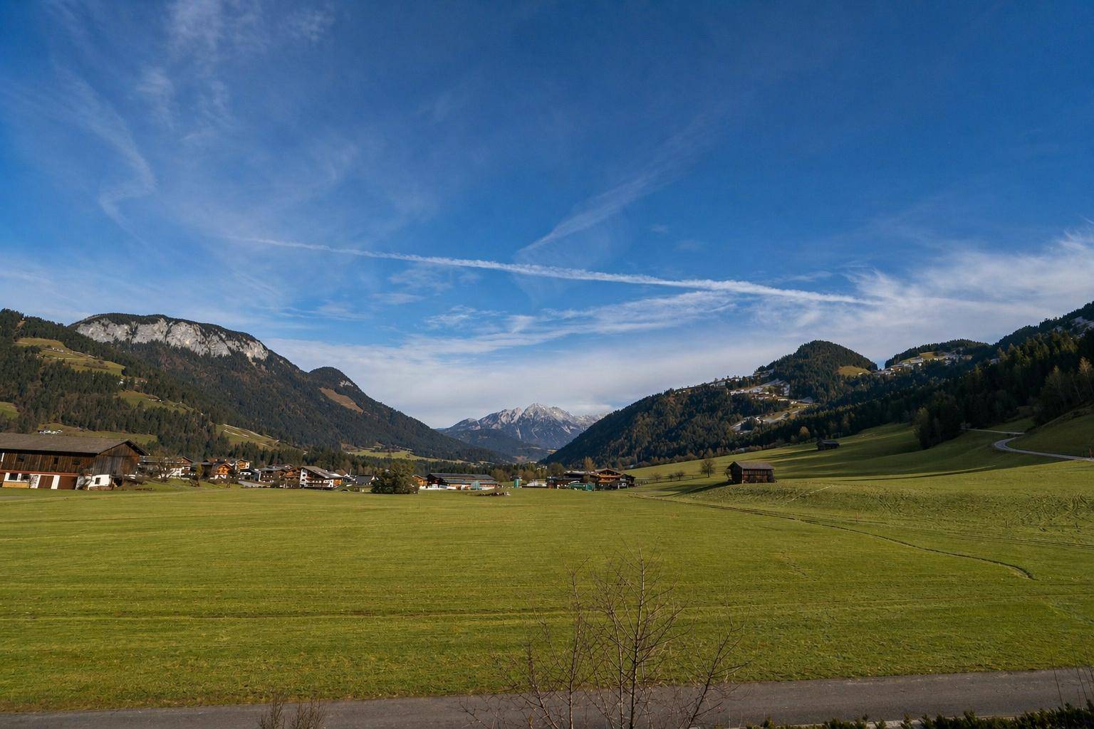 Weitläufige grüne Landschaft mit sanften Hügeln und majestätischen Bergen unter blauem Himmel.