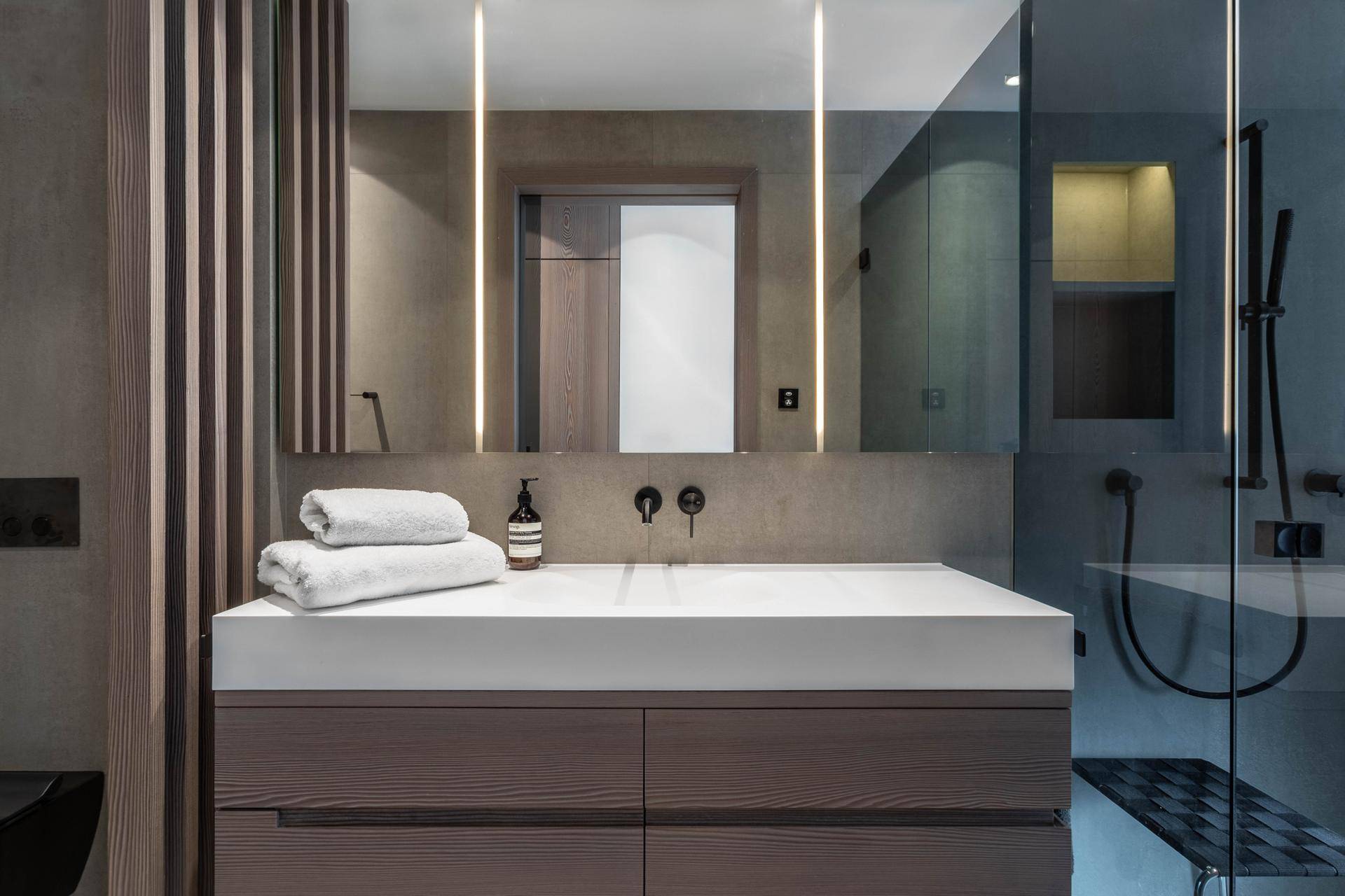 Modernes Badezimmer mit elegantem Waschtisch, beleuchtetem Spiegel und begehbarer Glasdusche.