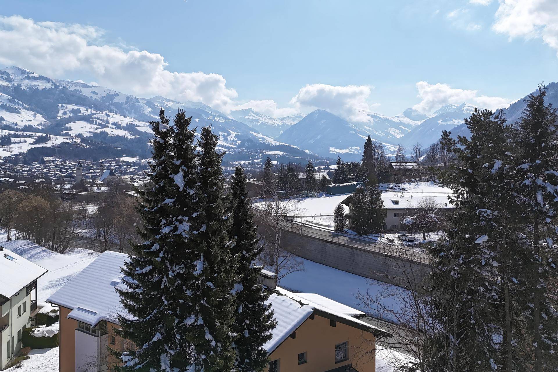 Panoramablick auf die schneebedeckten Alpen und das Tal mit Häusern und Bäumen.