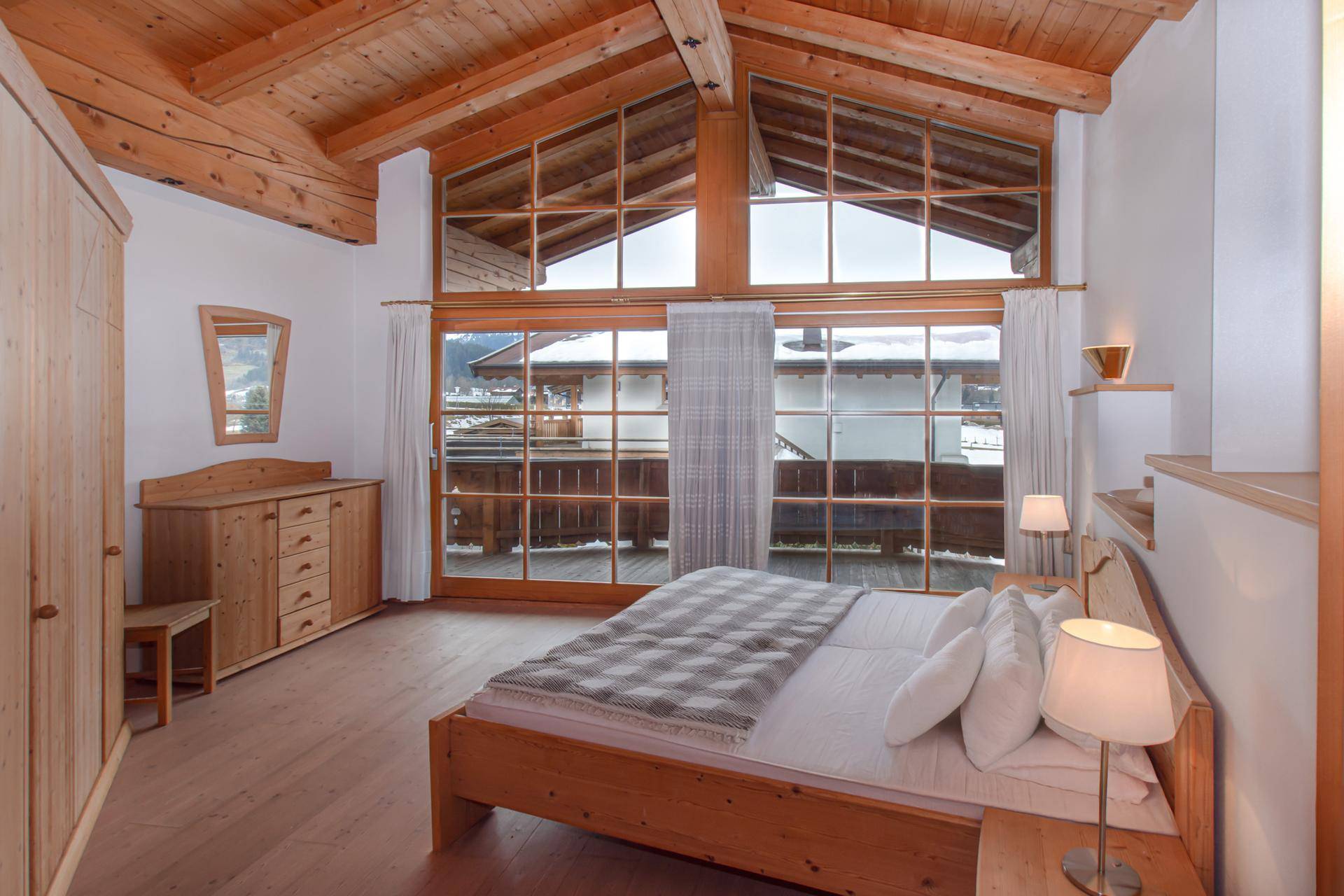 Geräumiges Schlafzimmer mit Holzbalkendecke, großen Fenstern und Zugang zum Balkon.
