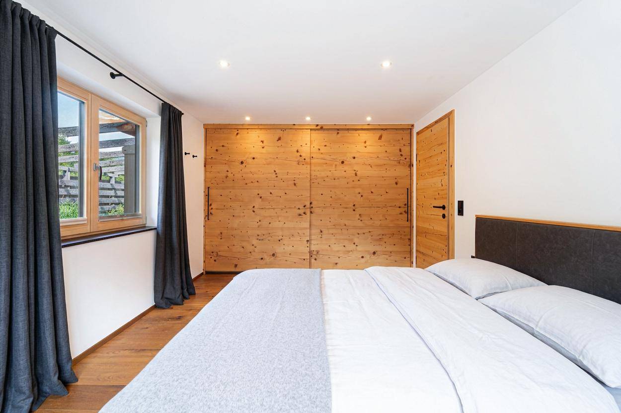 Helles Schlafzimmer mit Holzboden, großem Bett und integrierten Holzschränken, Blick ins Grüne.