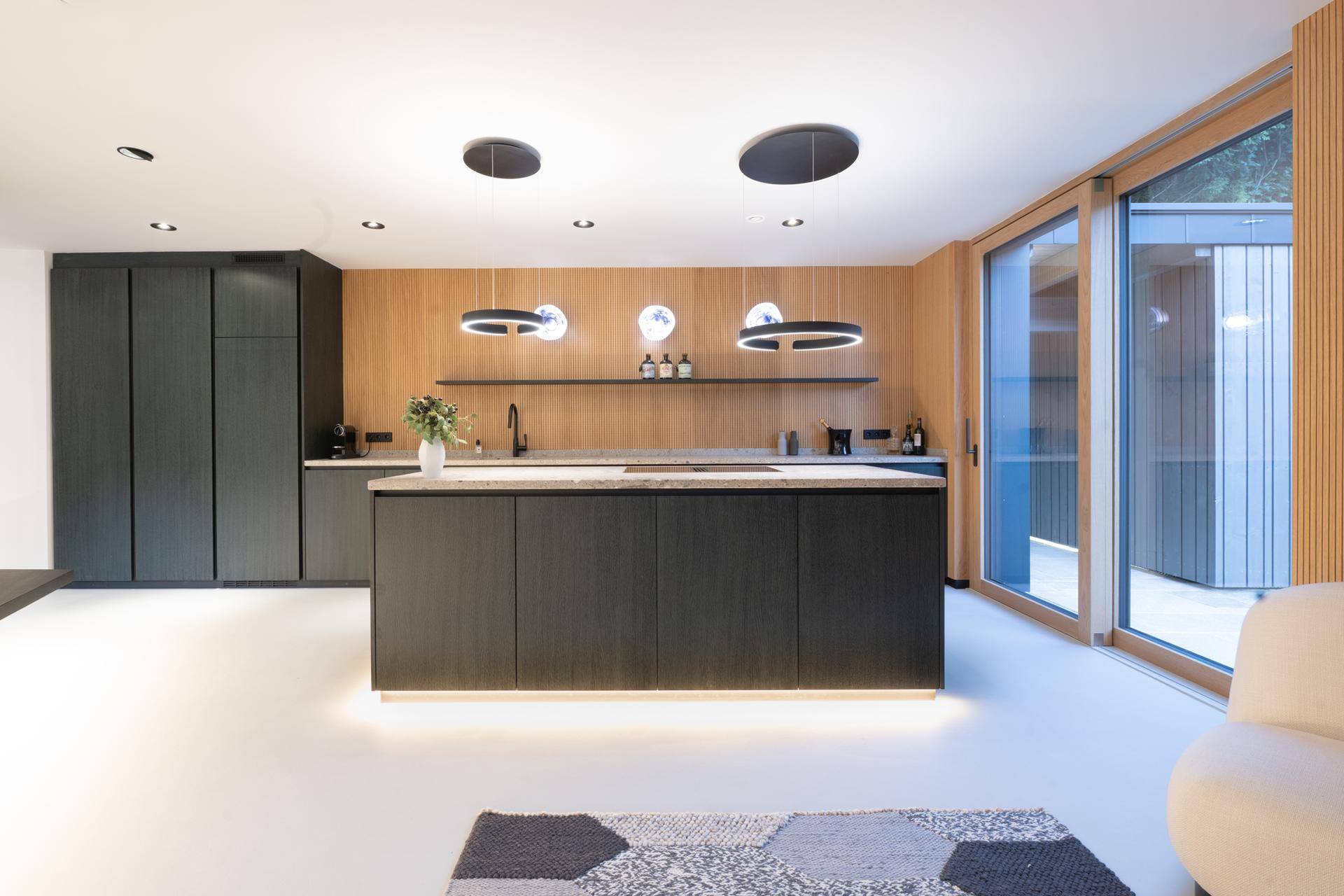 Elegante Küche mit dunklen Schränken, beleuchteter Insel und großen Glasfronten.