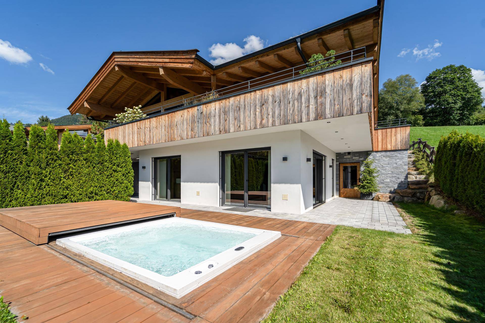 Außenbereich mit modernem Whirlpool auf Holzdeck, kleiner Rasenfläche und Zugang zum Haus.