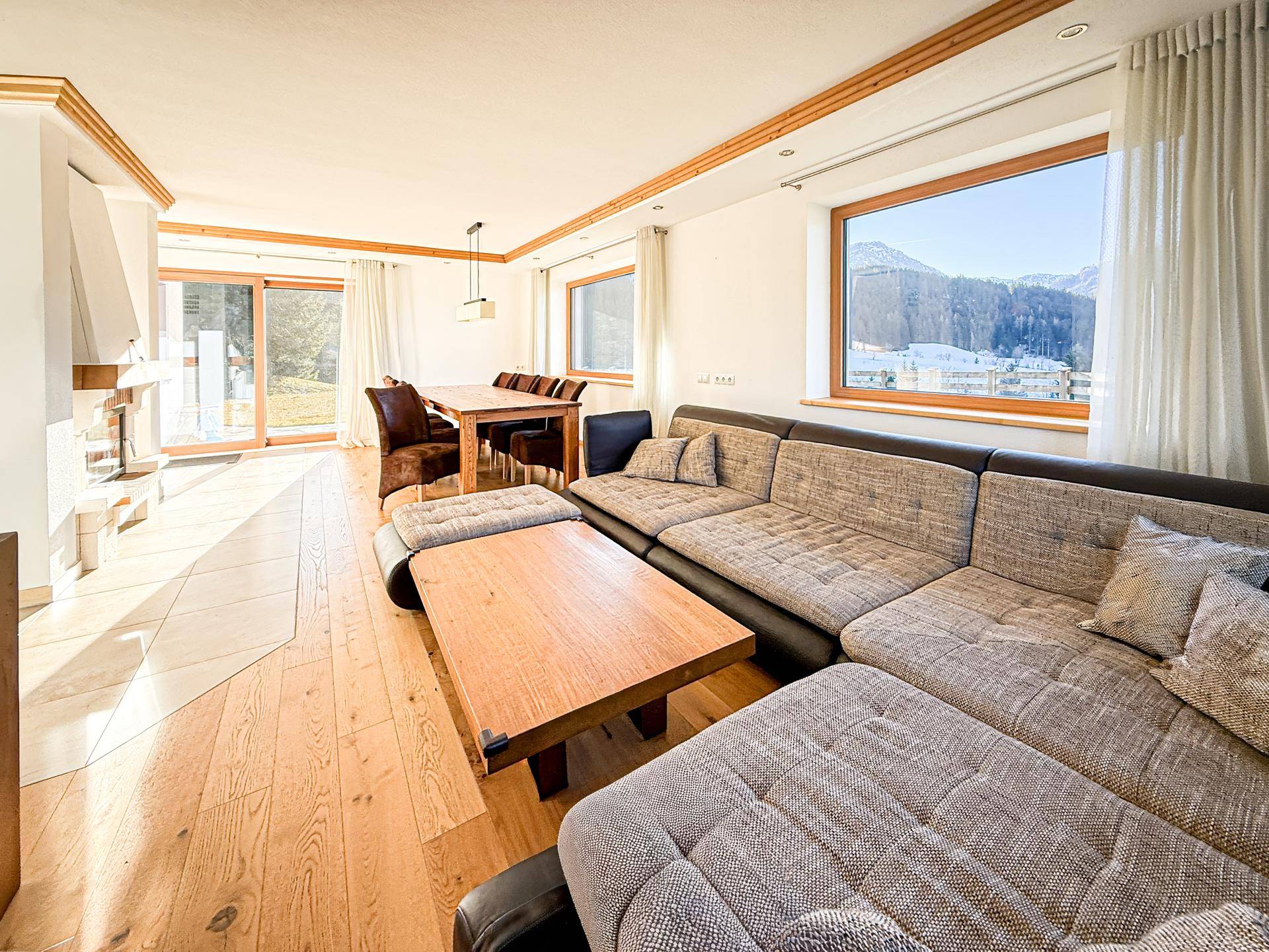 Heller Wohn-Essbereich mit Holzboden, großem Sofa und Bergblick durch die Fenster.