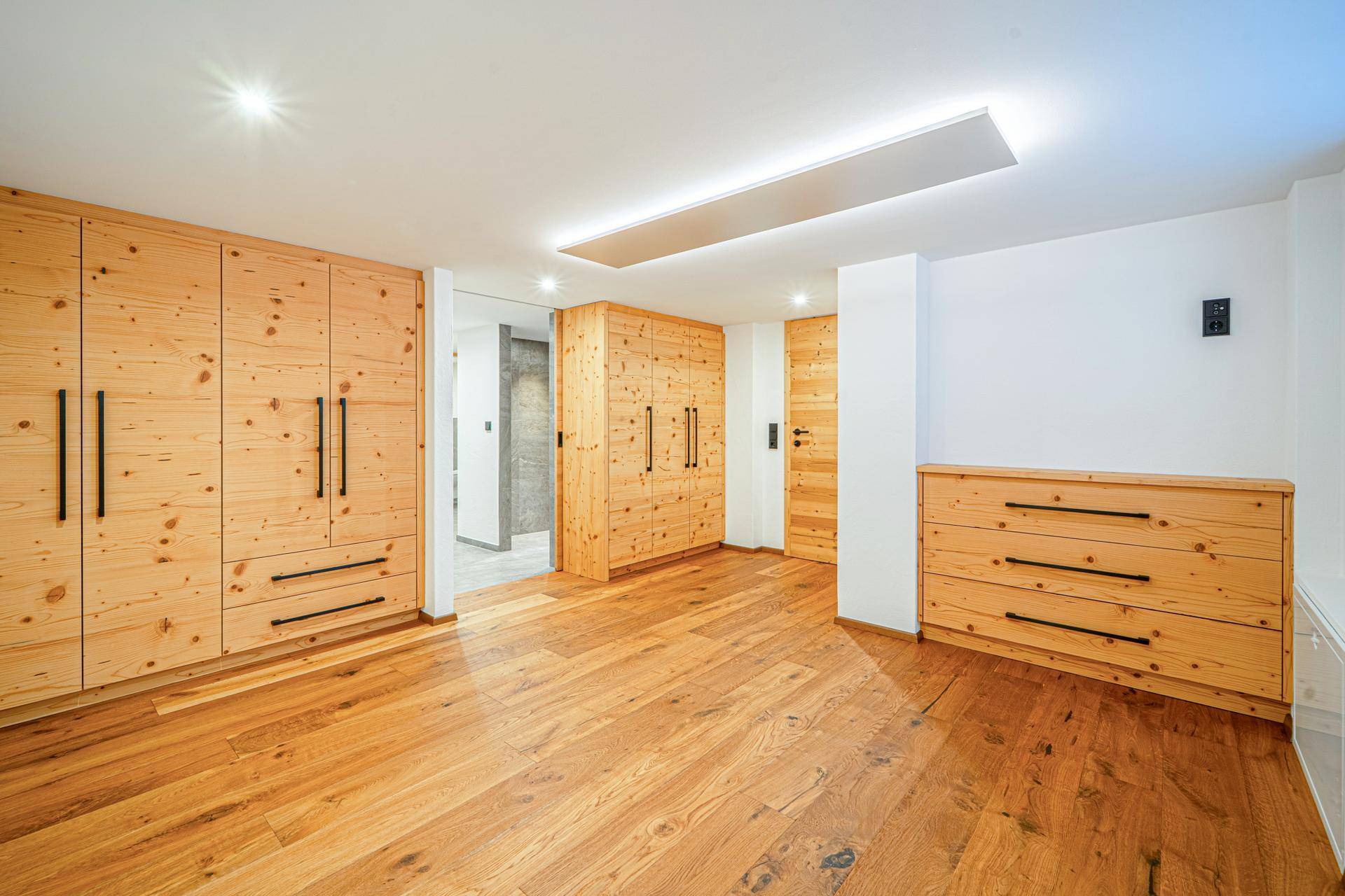Geräumiges Schlafzimmer mit Holzboden und vielen Einbauschränken aus hellem Holz, modern beleuchtet.