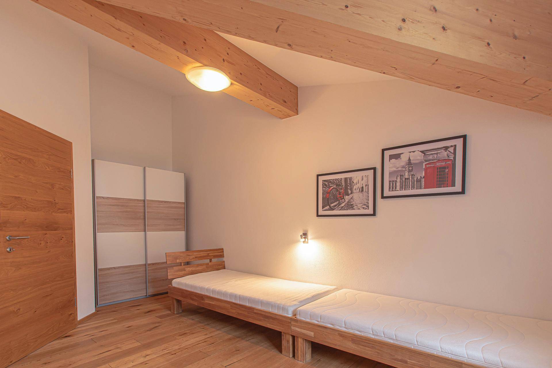 Helles Schlafzimmer mit zwei Einzelbetten, Holzfußboden und praktischem Schiebetürenschrank.