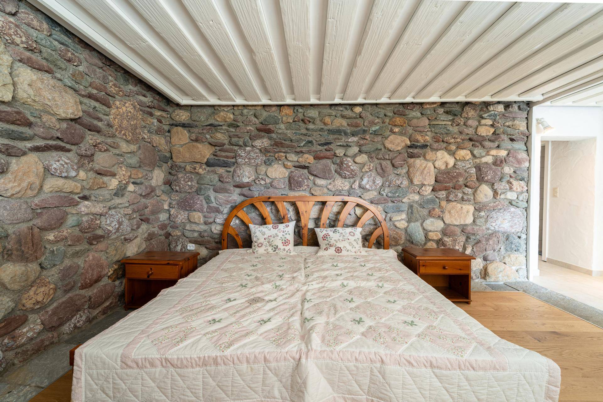 Rustikales Schlafzimmer mit Steinwand, Holzbalkendecke und Doppelbett.