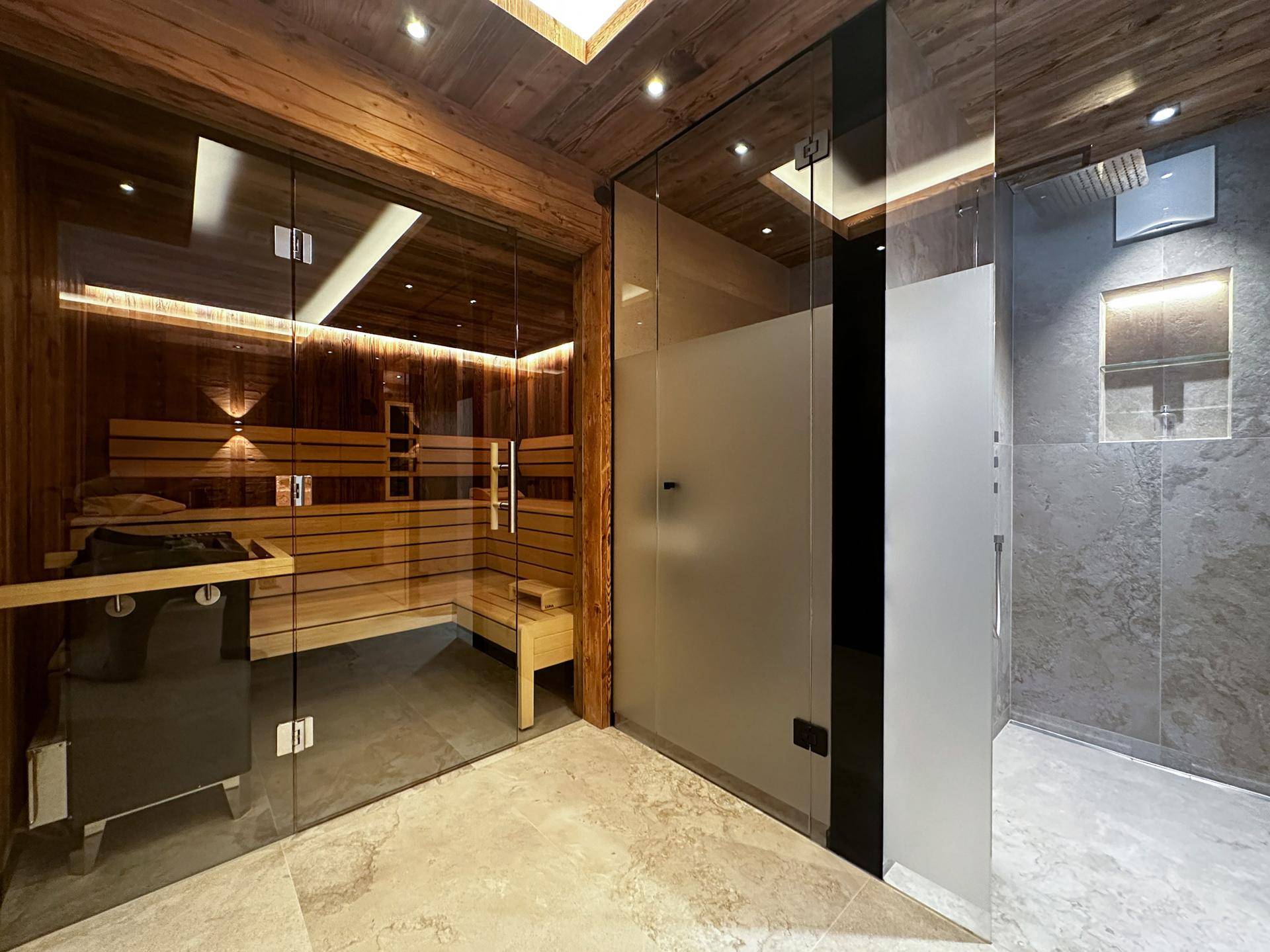 Exklusiver Wellnessbereich mit Sauna und moderner Dusche, umgeben von Holzelementen und Fliesen.