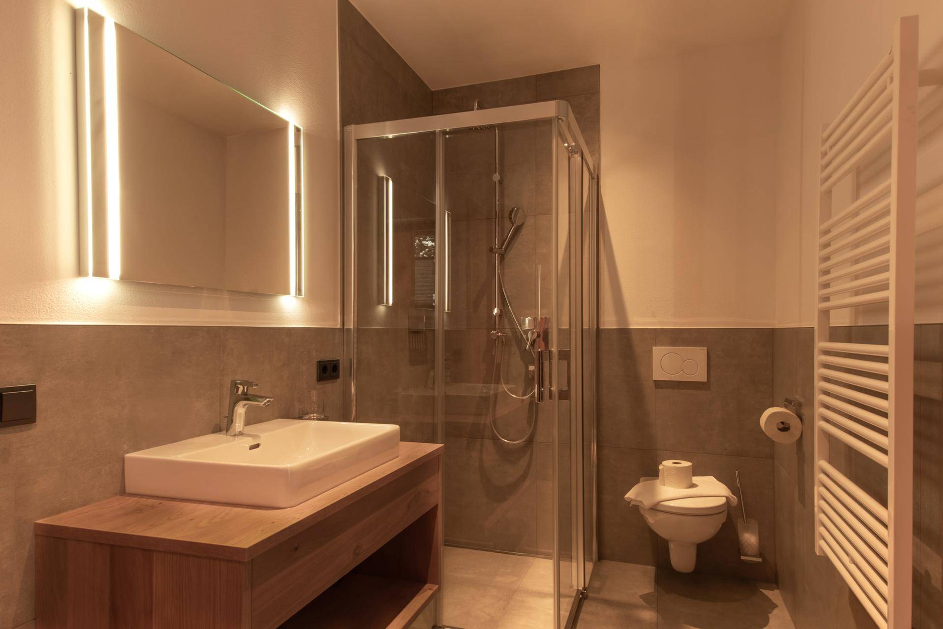 Modernes Badezimmer mit Dusche, Einzelwaschbecken und beheiztem Handtuchhalter.