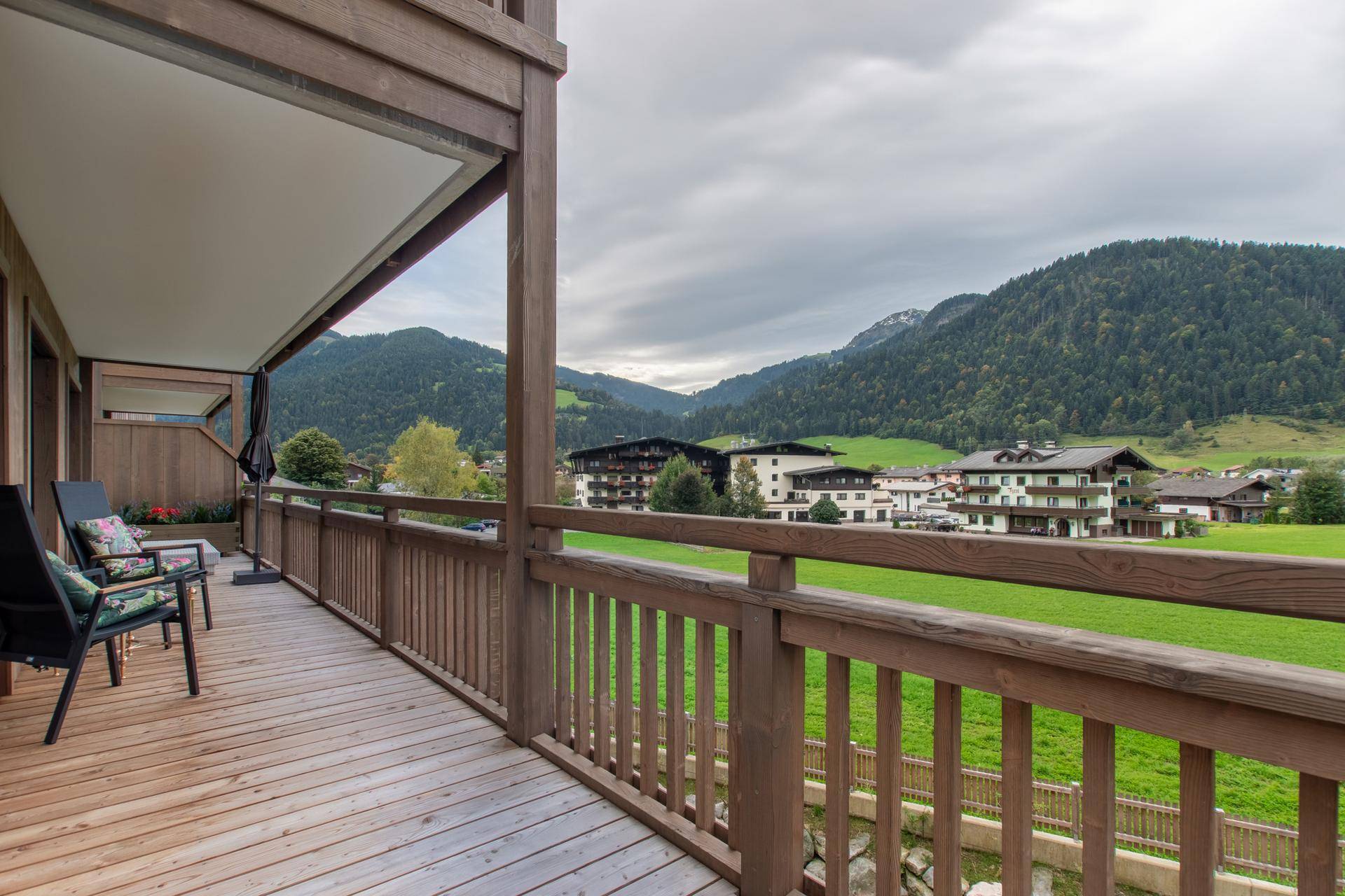 Großer Balkon mit Holzboden und Sitzgelegenheiten, bietet einen weiten Blick auf die grüne Landschaft und Berge.