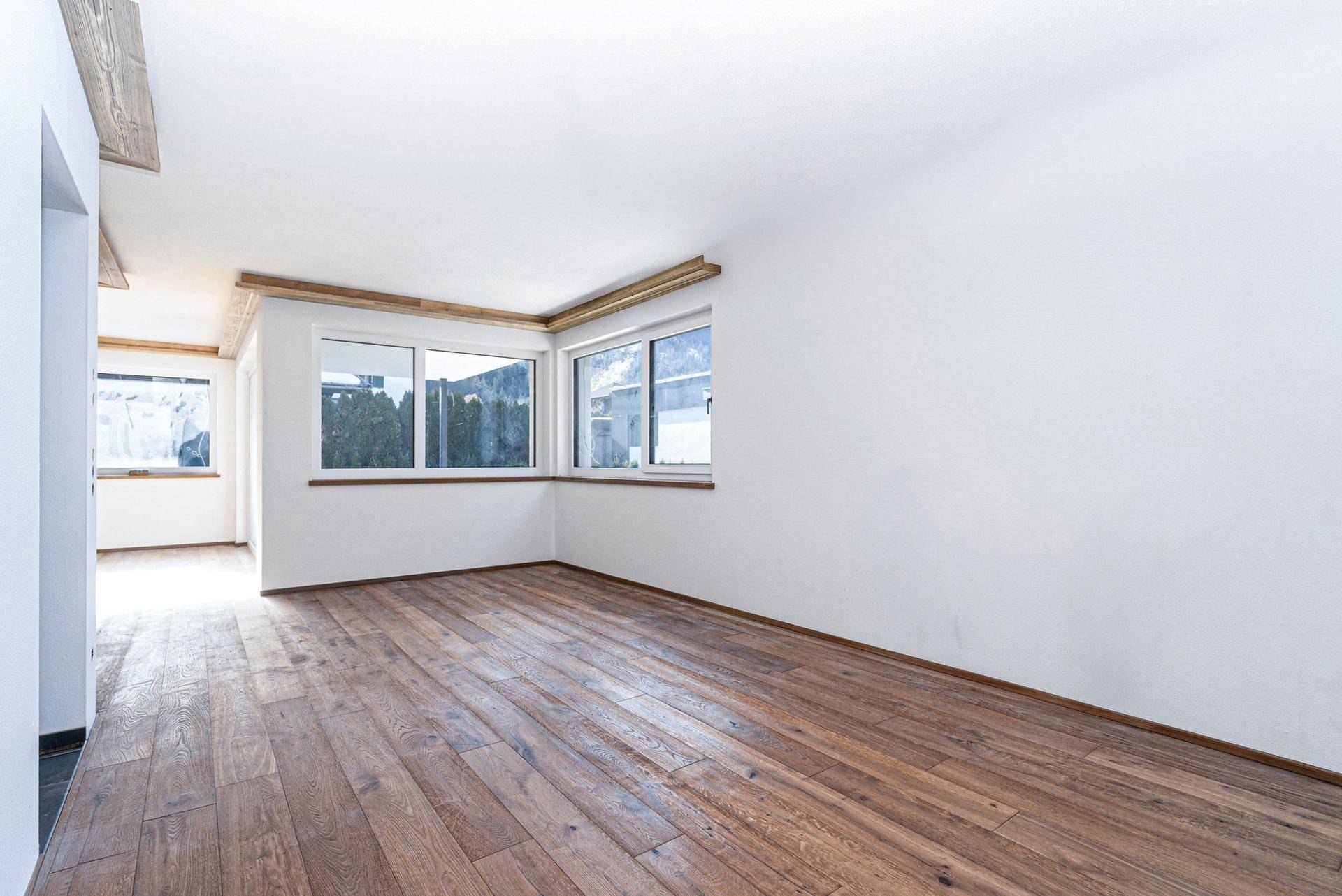 Geräumiger, leerer Raum mit Holzboden und mehreren Fenstern, die viel Tageslicht hereinlassen.