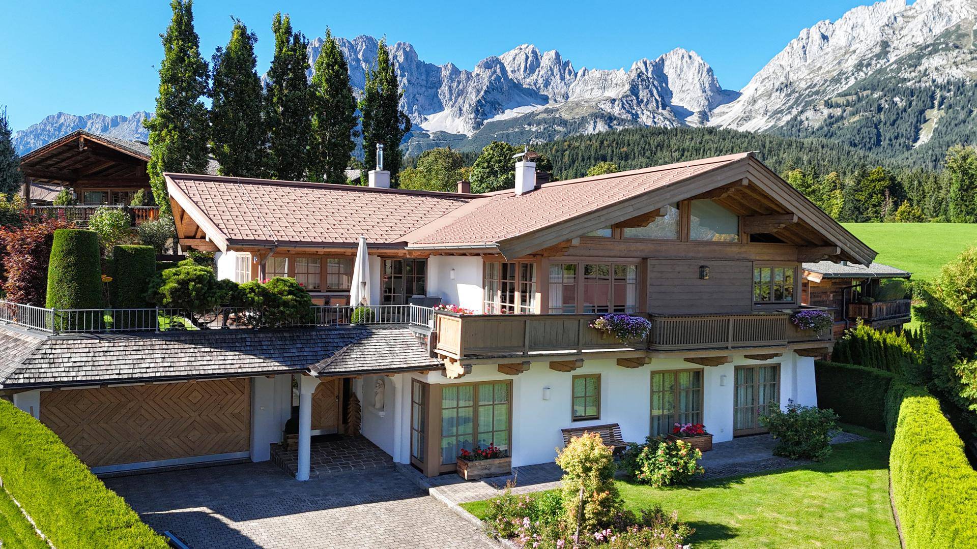 Malerisches Landhaus mit Satteldach und Balkonen, eingebettet in eine grüne Landschaft mit majestätischem Bergpanorama.