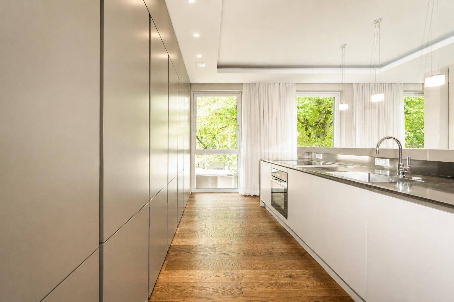 Moderne Küche mit integrierten Geräten, Holzboden und viel Tageslicht durch große Fenster.