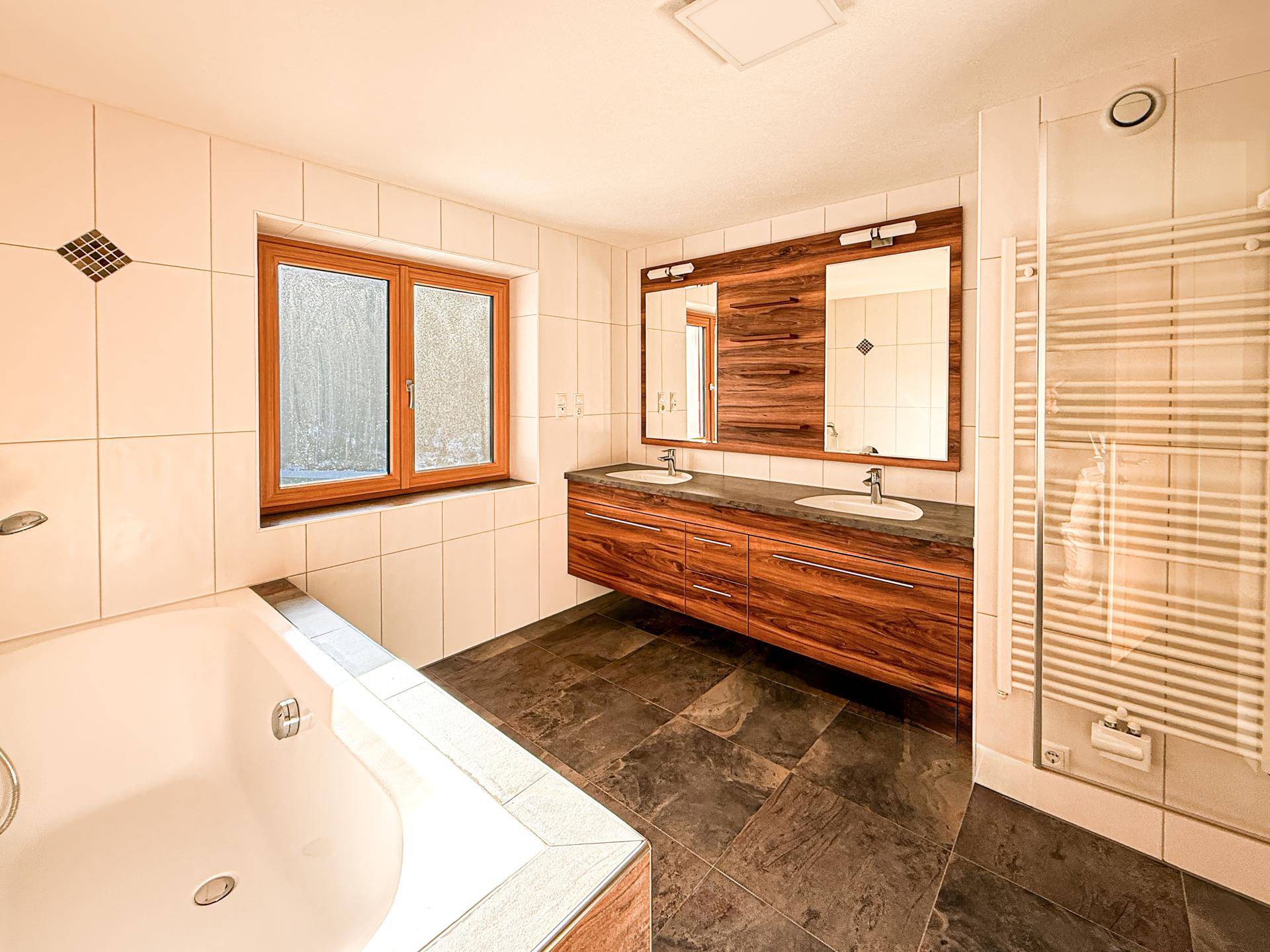 Modernes Badezimmer mit Badewanne, Doppelwaschbecken und dunklem Fliesenboden.