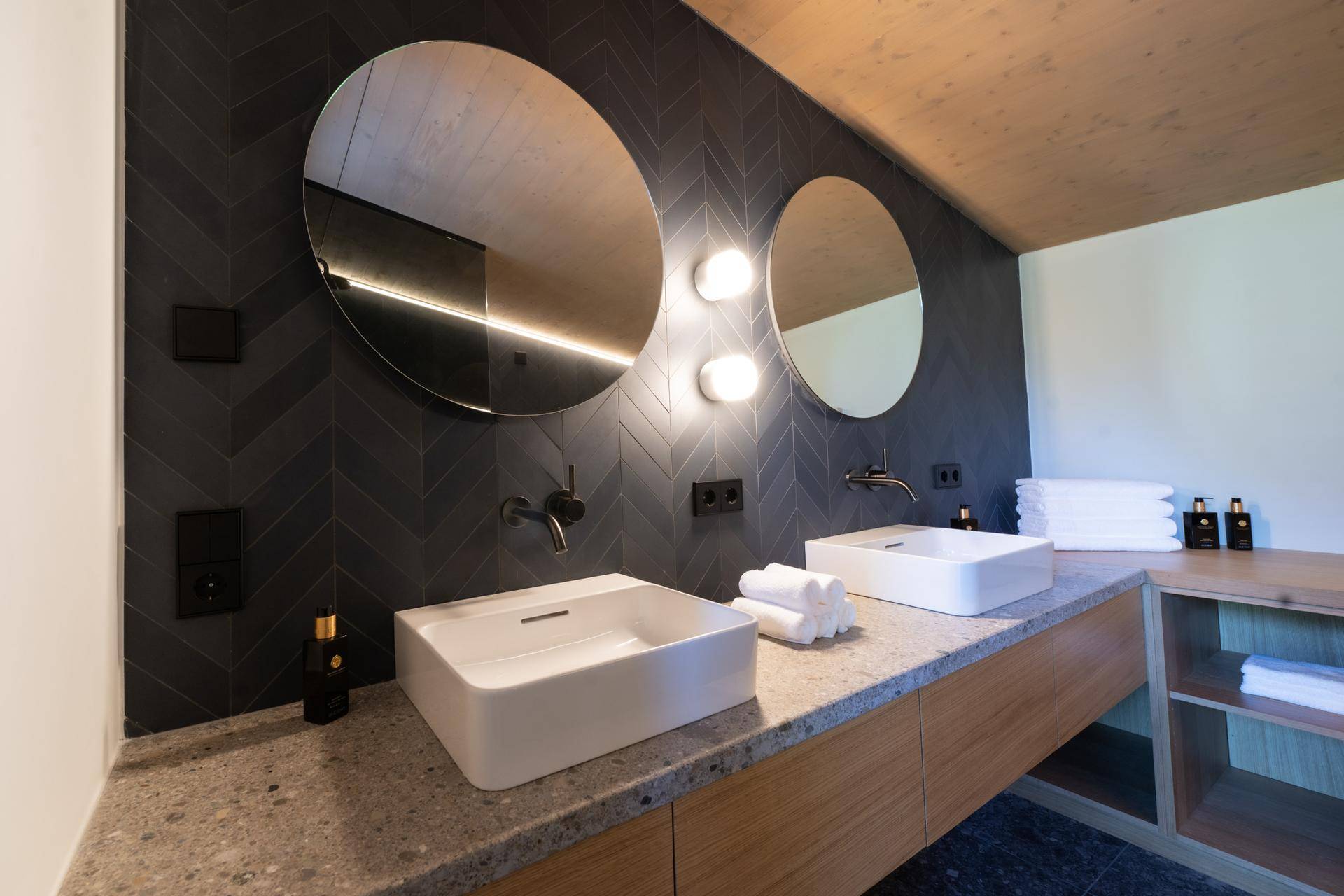 Modernes Badezimmer mit Doppelwaschbecken, runden Spiegeln und dunklen Fliesen.