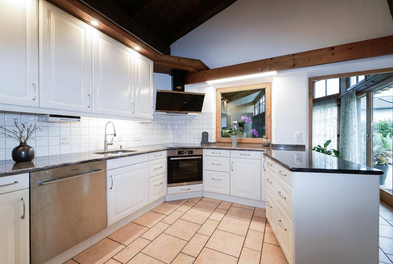Moderne Einbauküche mit weißen Schränken, dunklen Arbeitsplatten und Fliesenboden.