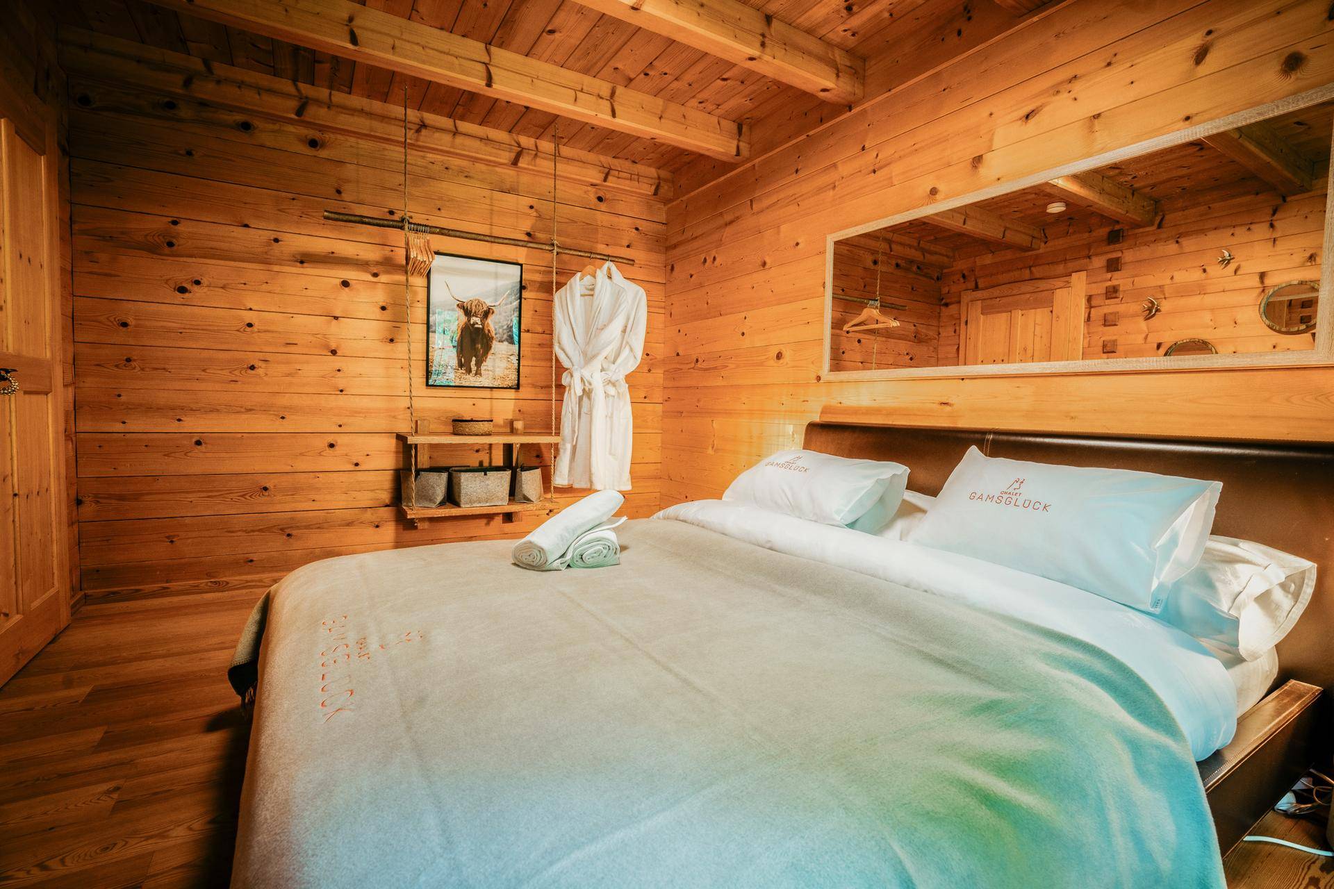 Gemütliches Schlafzimmer mit Holzwänden, Holzboden und einem großen Spiegel über dem Bett im alpinen Stil.