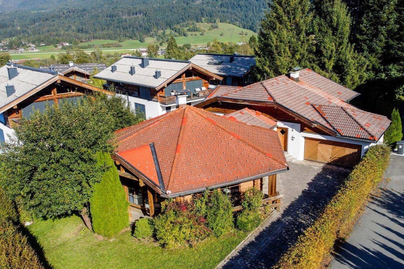 Luftaufnahme des Anwesens mit Chalet-Haus, Garage und umliegender Wohnbebauung in alpiner Landschaft.
