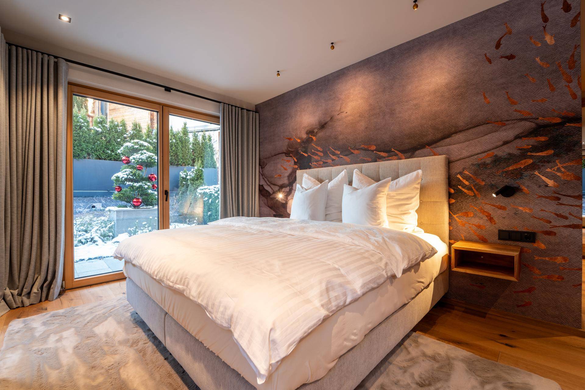 Helles Schlafzimmer mit großem Bett, dekorativer Wandgestaltung und direktem Zugang zum Garten.