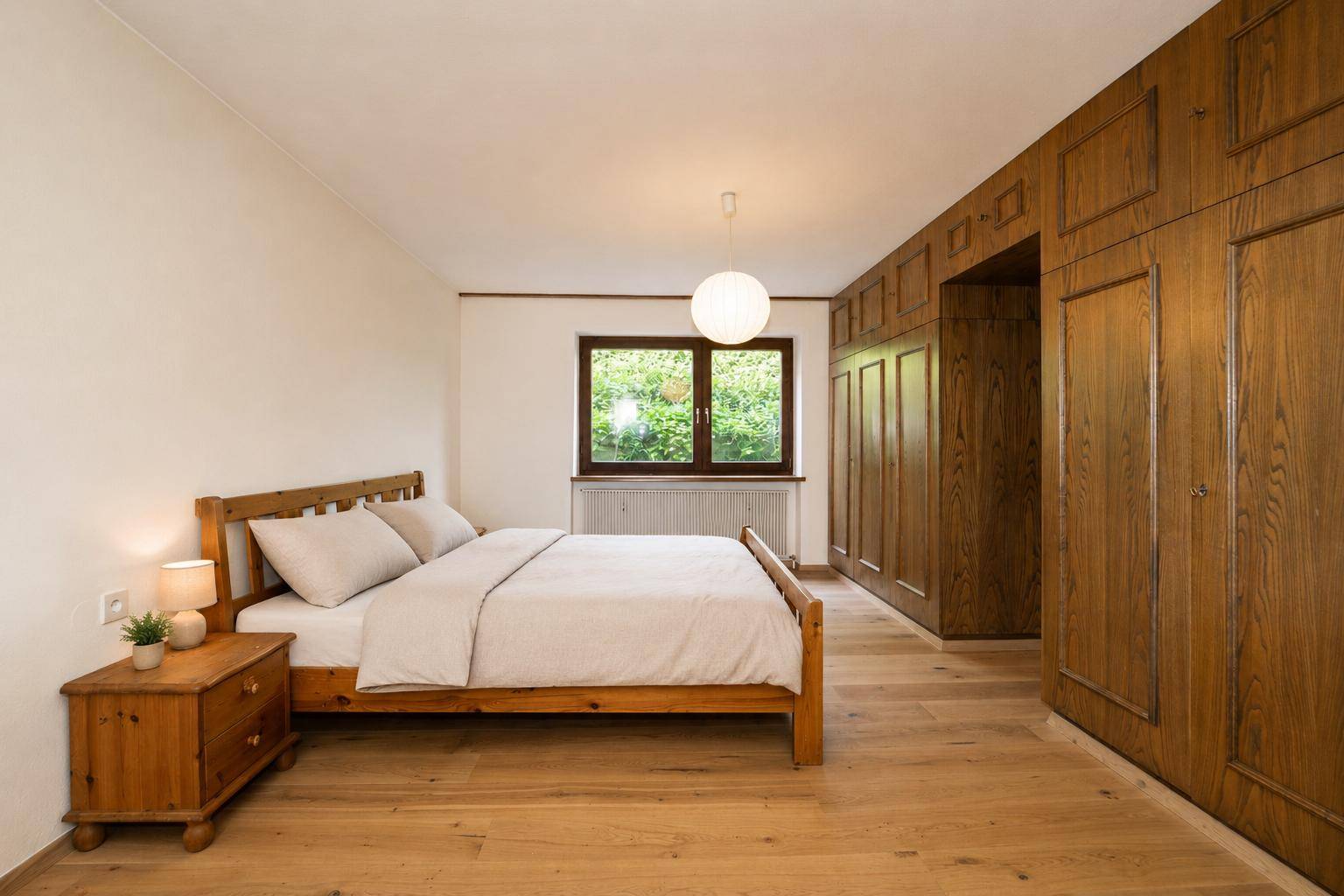 Schlafzimmer mit Holzbett, Einbauschränken aus Holz und hellem Holzboden.