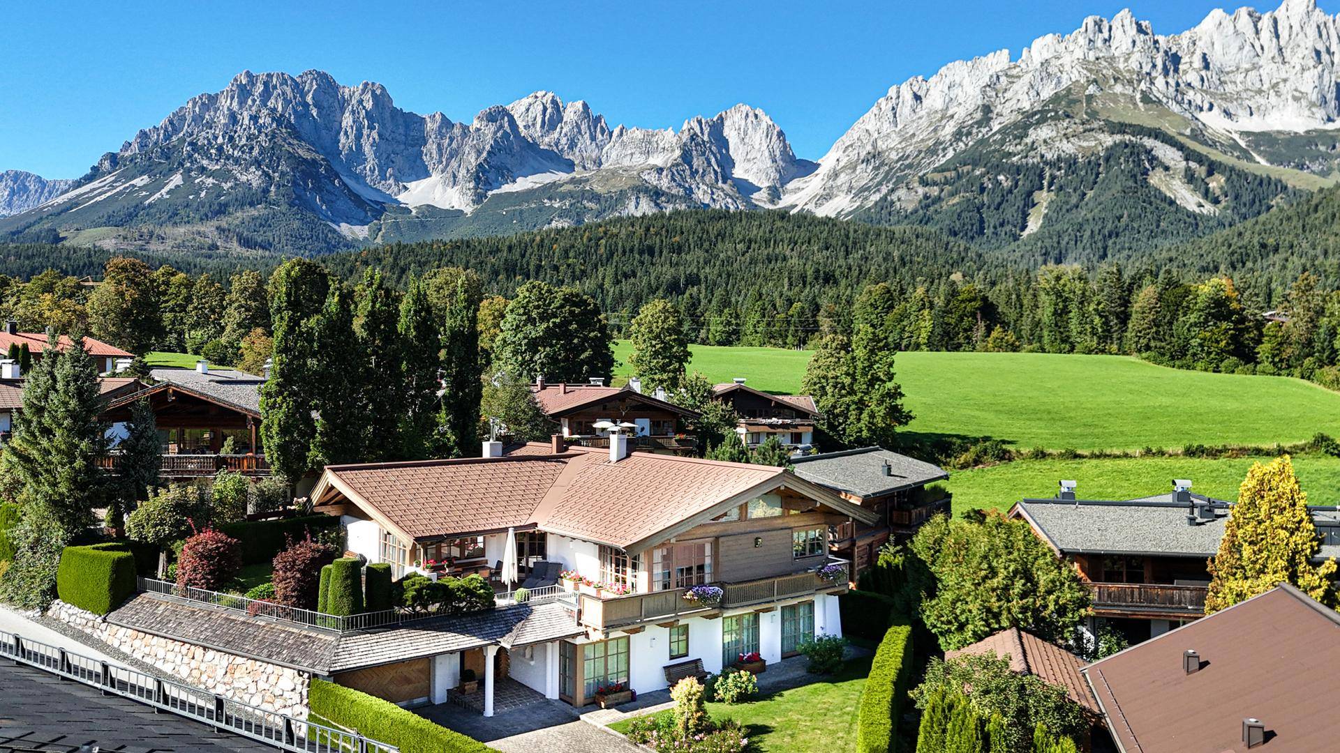 Weitläufige Ansicht eines Wohngebiets mit traditionellen Häusern vor einer beeindruckenden Bergkette und Wäldern.