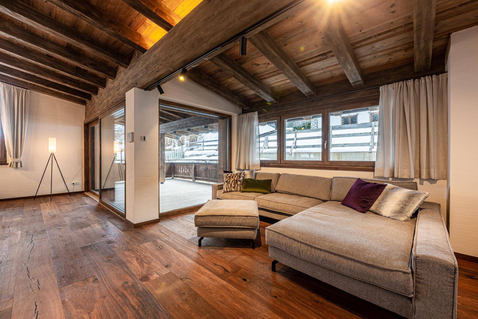 Helles Wohnzimmer mit Holzbalkendecke, bequemer Couch und Zugang zur Terrasse.