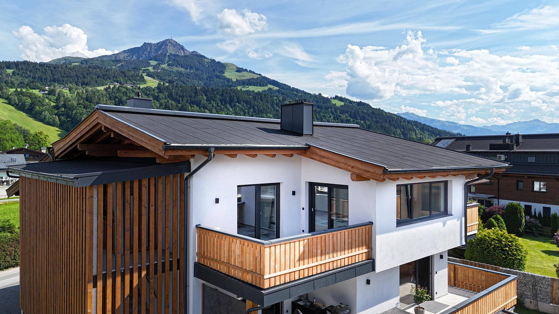 Moderne Architektur mit Holzverkleidung und Balkon vor einer beeindruckenden Bergkulisse.