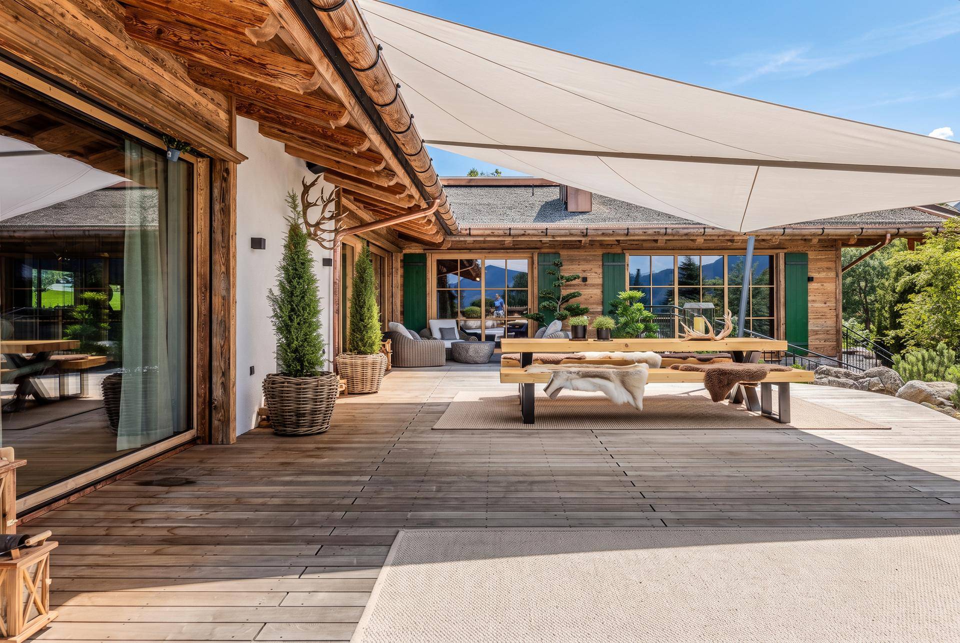 Geräumige Holzterrasse mit Esstisch, Sonnensegel und Blick auf die umliegende Natur.