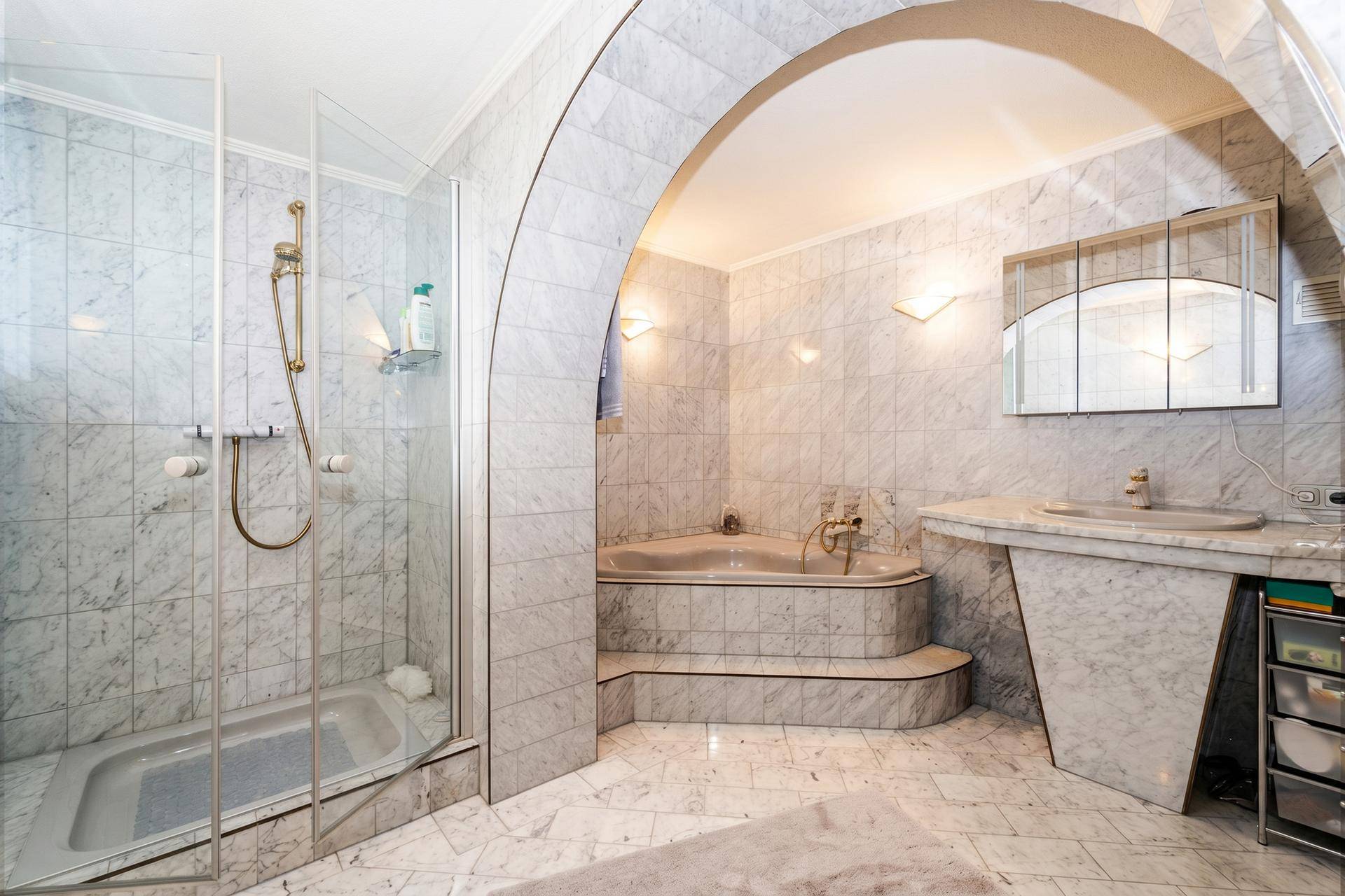 Geräumiges Badezimmer mit Marmorfliesen, Dusche und Eckbadewanne unter einem Bogen.