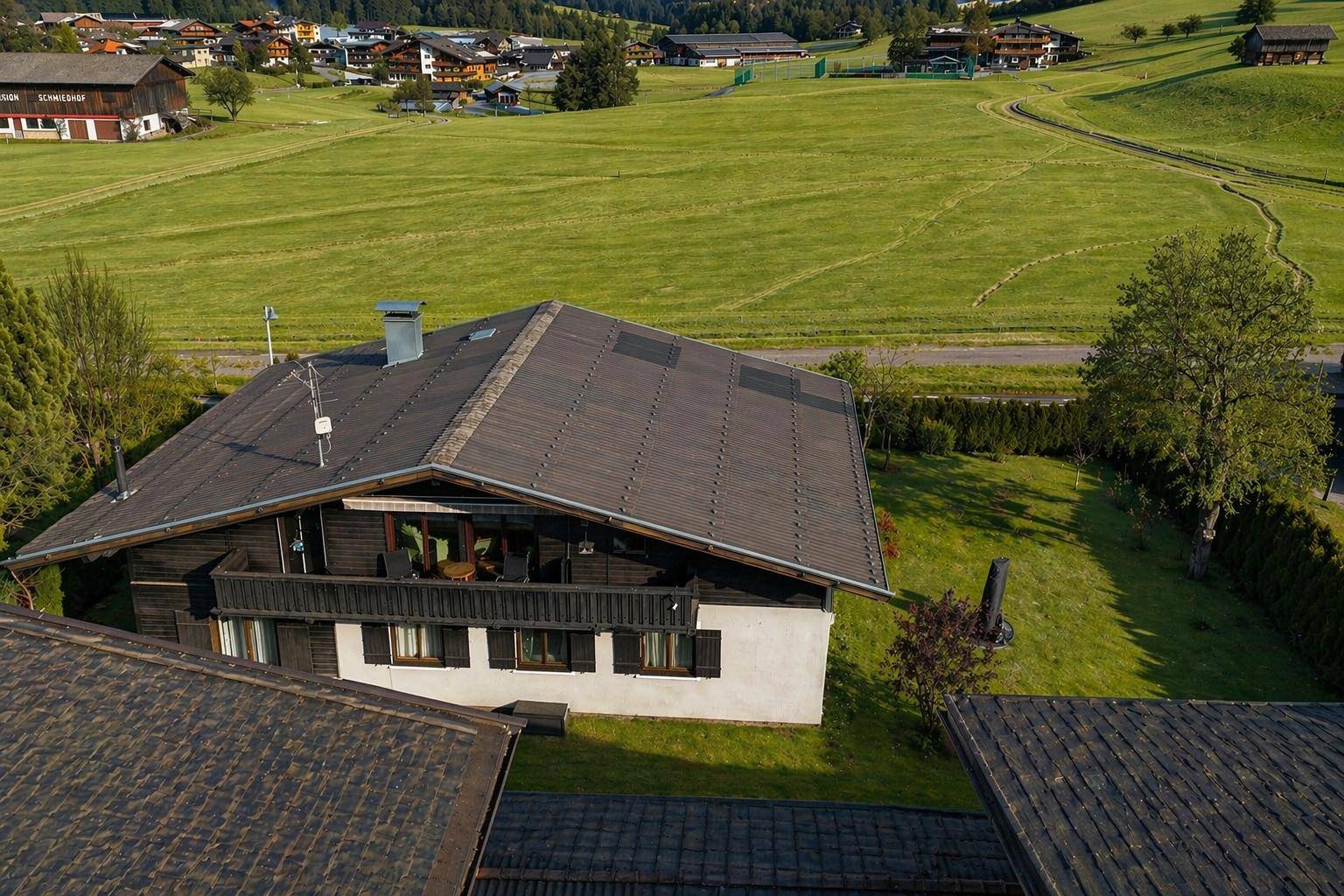 Luftaufnahme eines Hauses mit Satteldach und großem Garten, umgeben von grünen Wiesen.