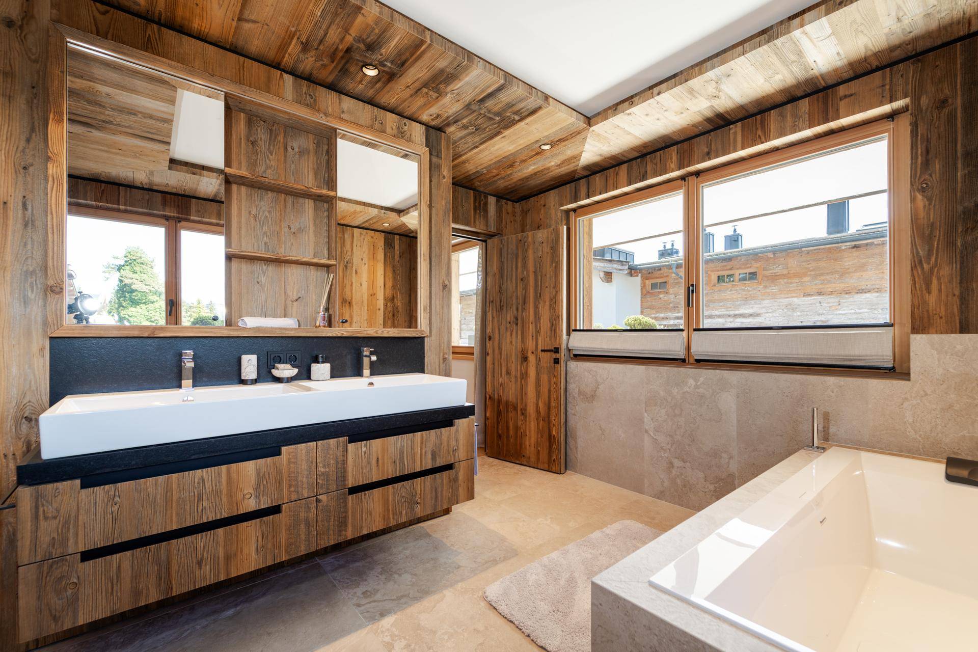 Modernes Badezimmer mit Doppelwaschbecken, Holzverkleidung, Badewanne und Fenster für Tageslicht.