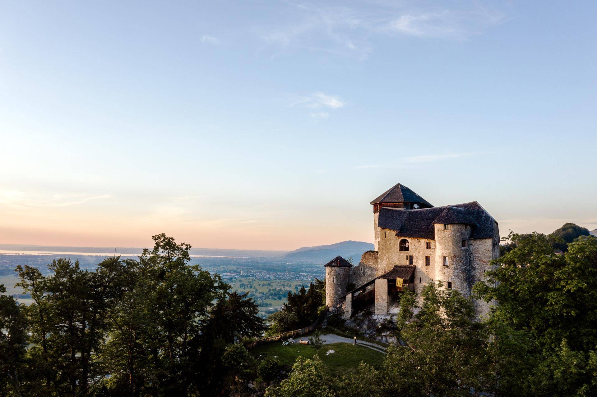 Historisches Schloss auf einem Hügel mit weitem Blick über die grüne Landschaft bei Sonnenuntergang.