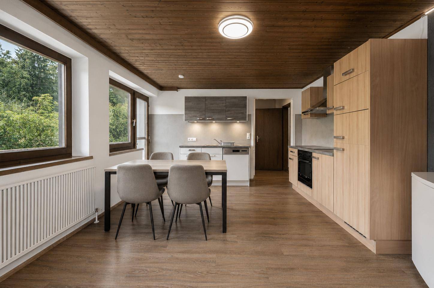 Offener Wohnbereich mit Essplatz, moderner Küchenzeile und Holzdeckenverkleidung.