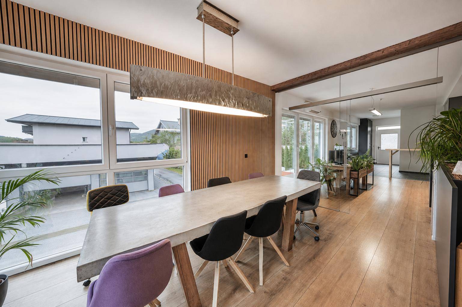 Großer Besprechungsraum mit modernem Tisch, Holzboden und vertikalen Holzlamellen an der Wand.