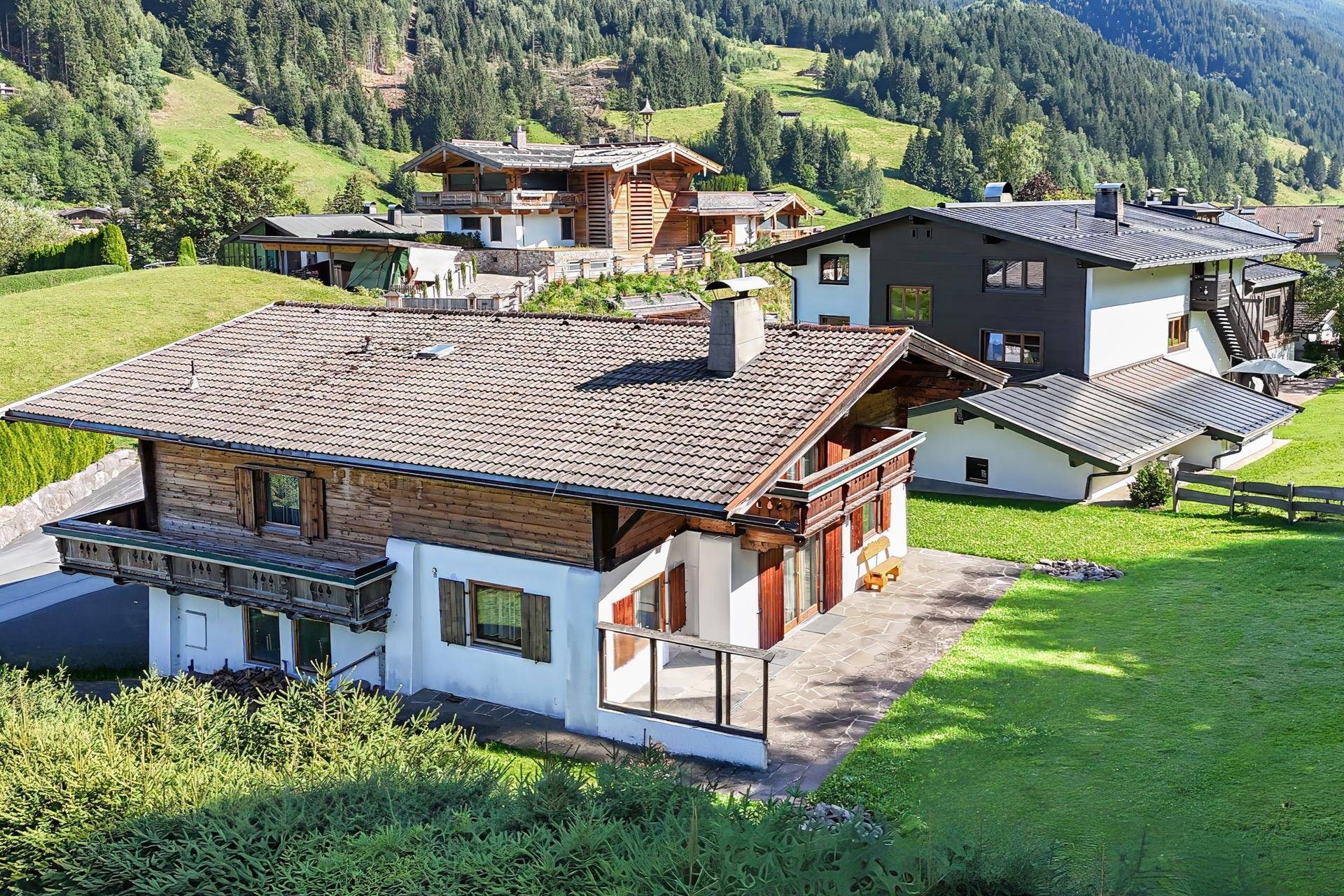Alpenländisches Haus in einer malerischen Wohngegend mit weiteren Gebäuden und grünen Hügeln im Hintergrund.